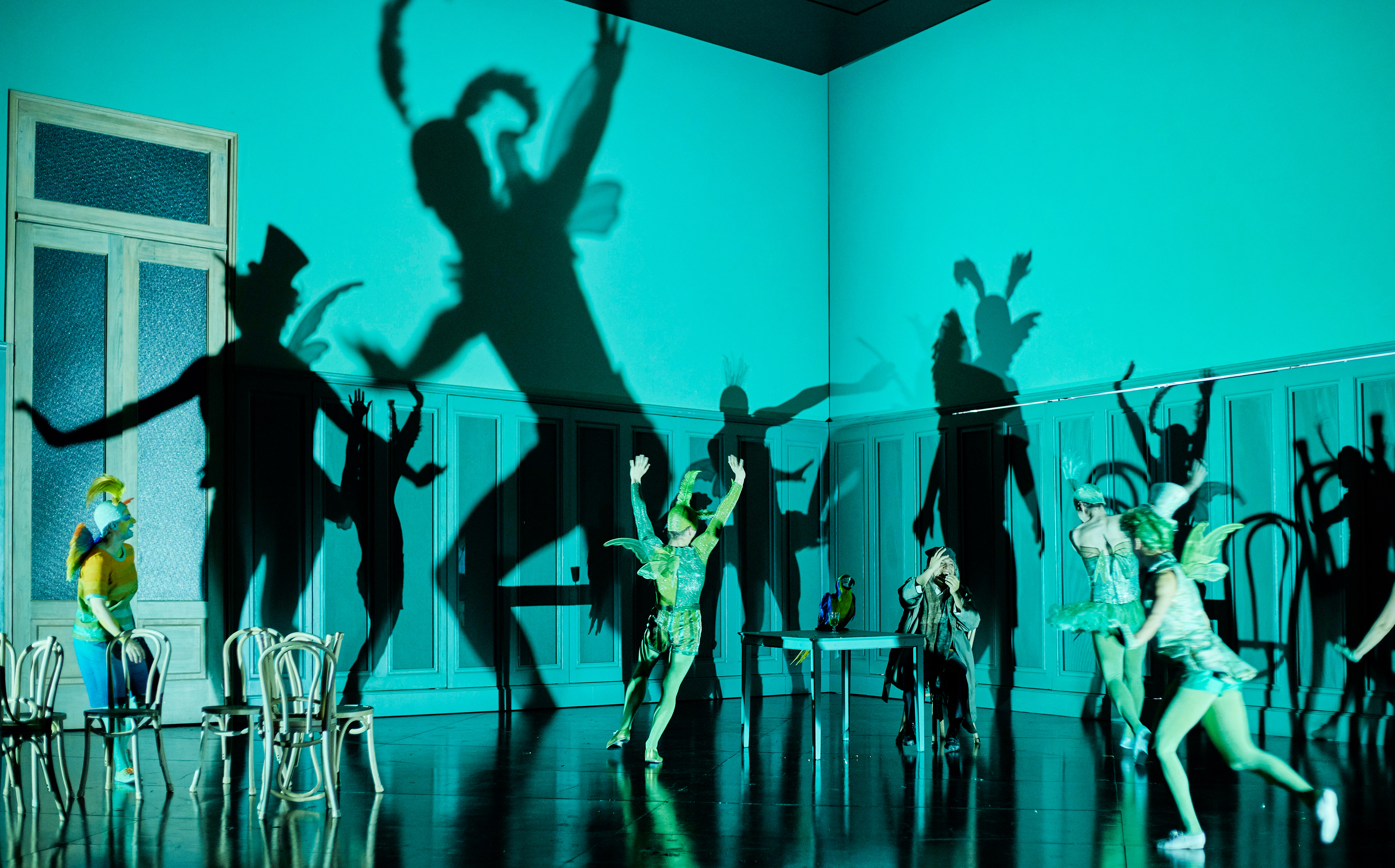 The Royal Opera perform The Tales of Hoffmann onstage. The stage is lit in a blue light and the singers shadows dominate the backdrop.
