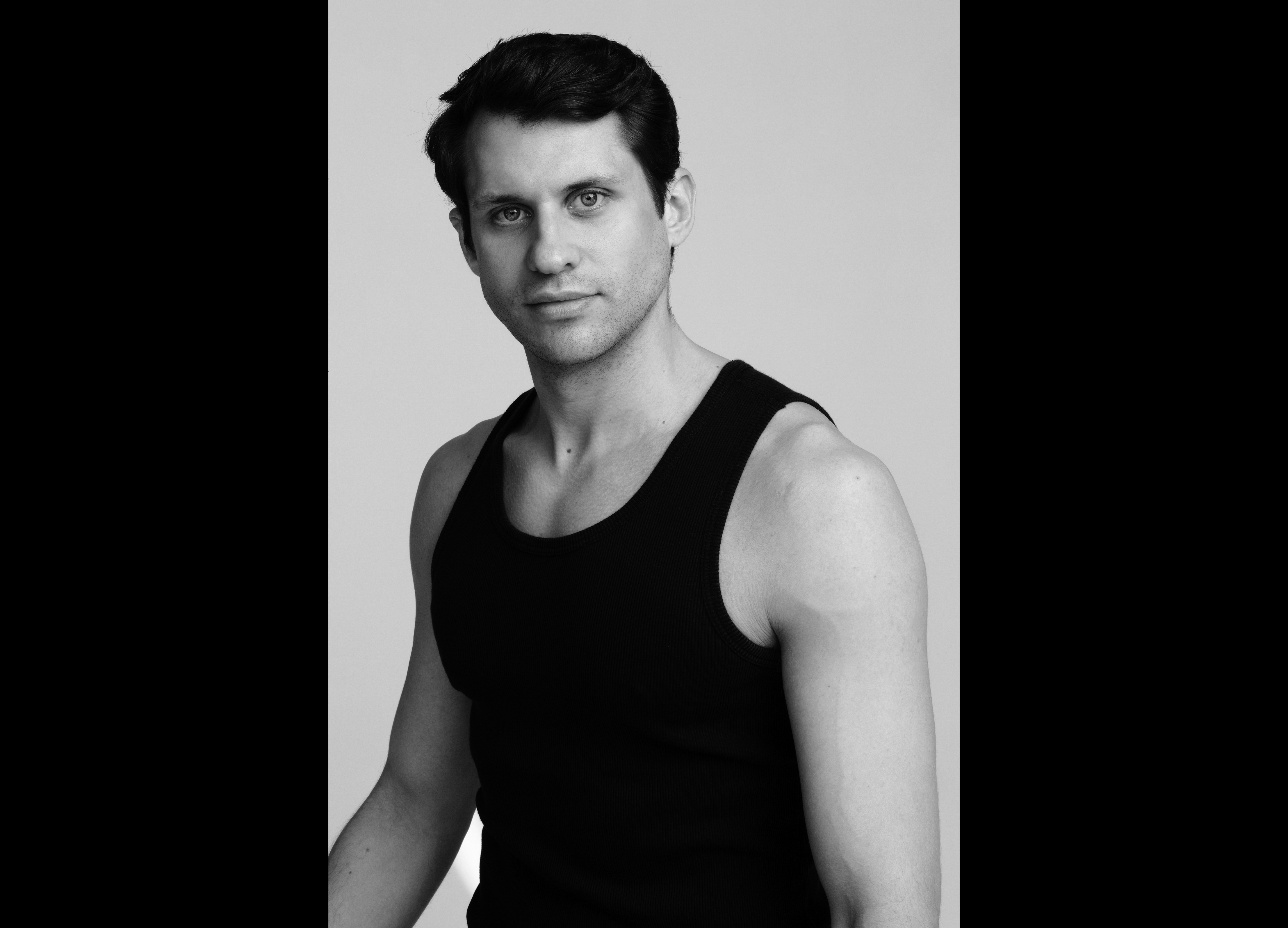 A black and white headshot of a person wearing a black vest. They are Nicol Edmonds, a first soloist of The Royal Ballet.