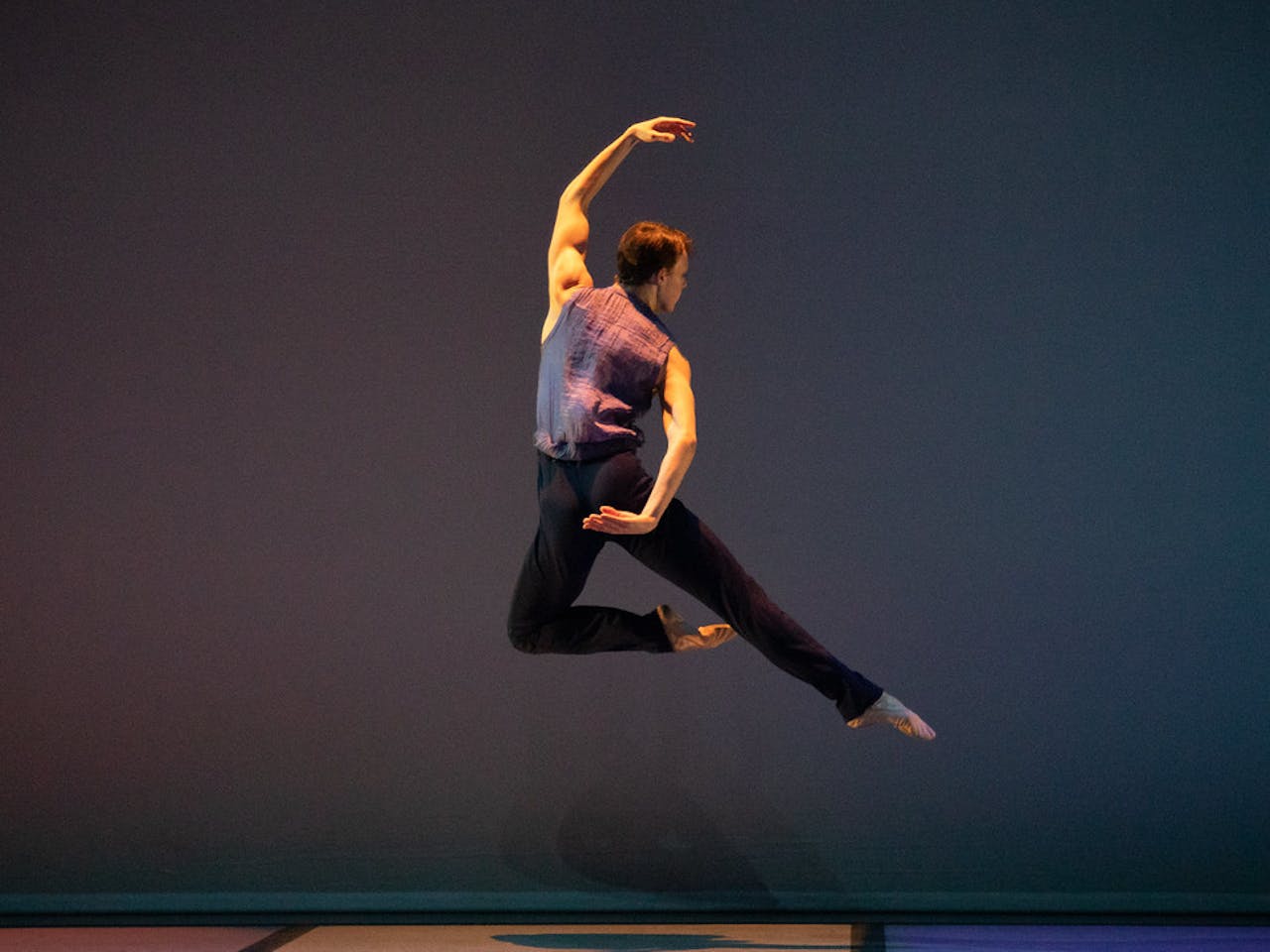 Ballet Dancer mid leap in front of blue background.
