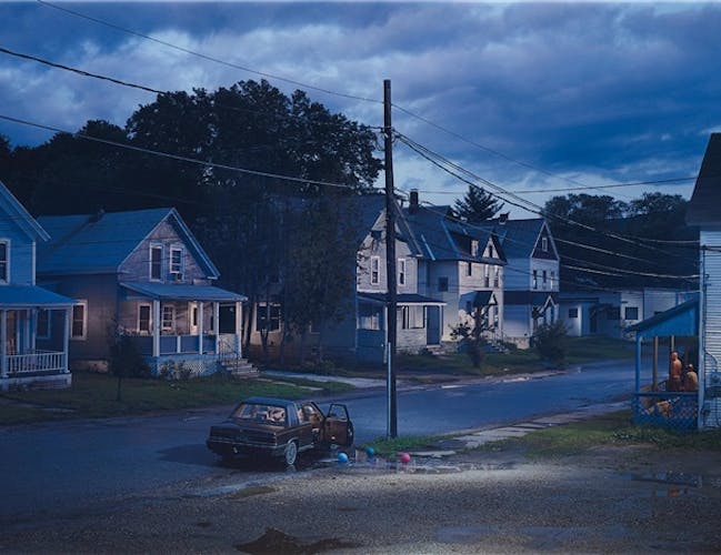 A photograph of a street darkened by the changing times. Large American style houses line the streets.