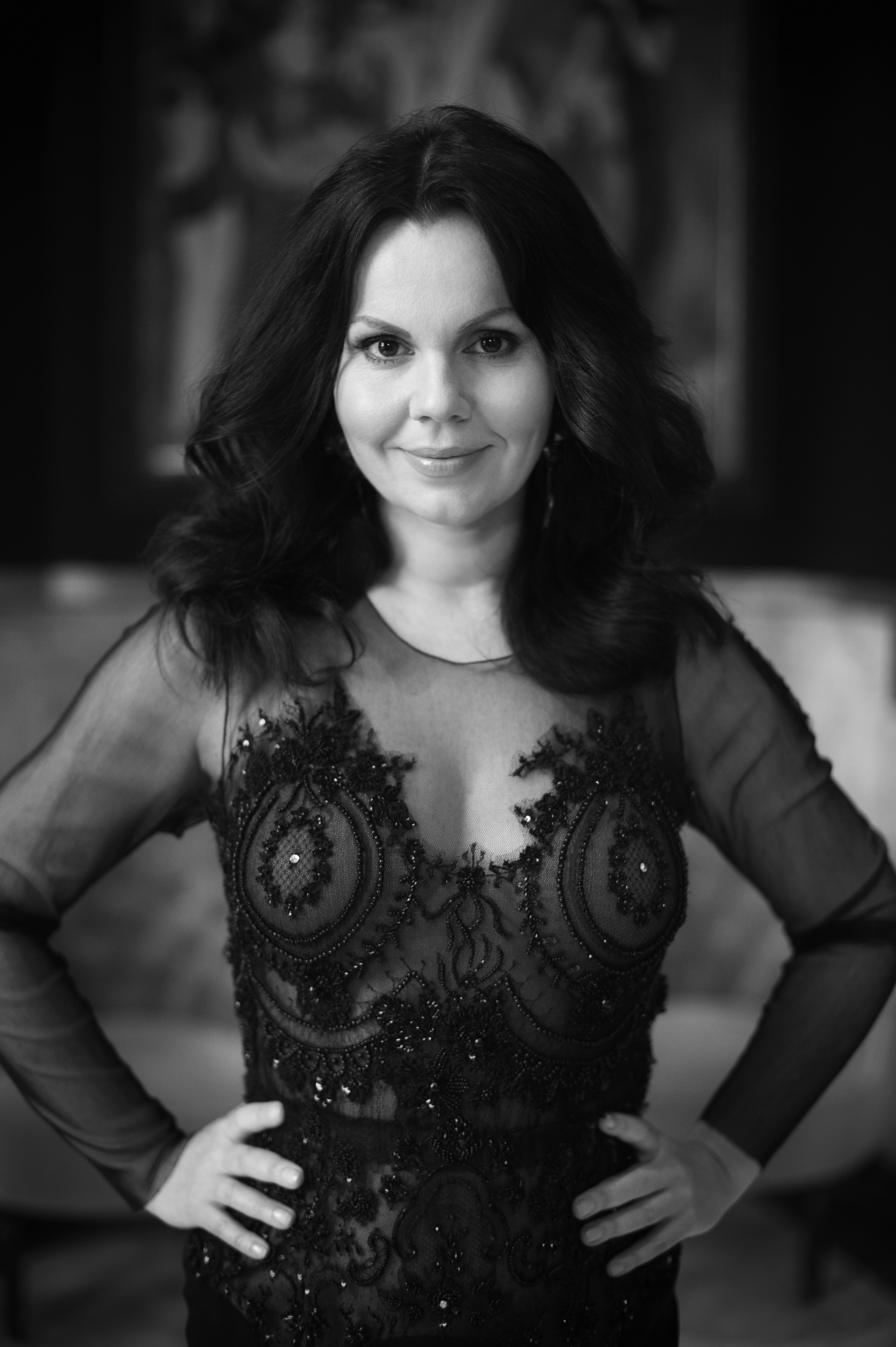 A black and white headshot of the opera singer Aleksandra Kurzak. Her long hair is worn down and she wears a sequinned dress with mesh arms. 