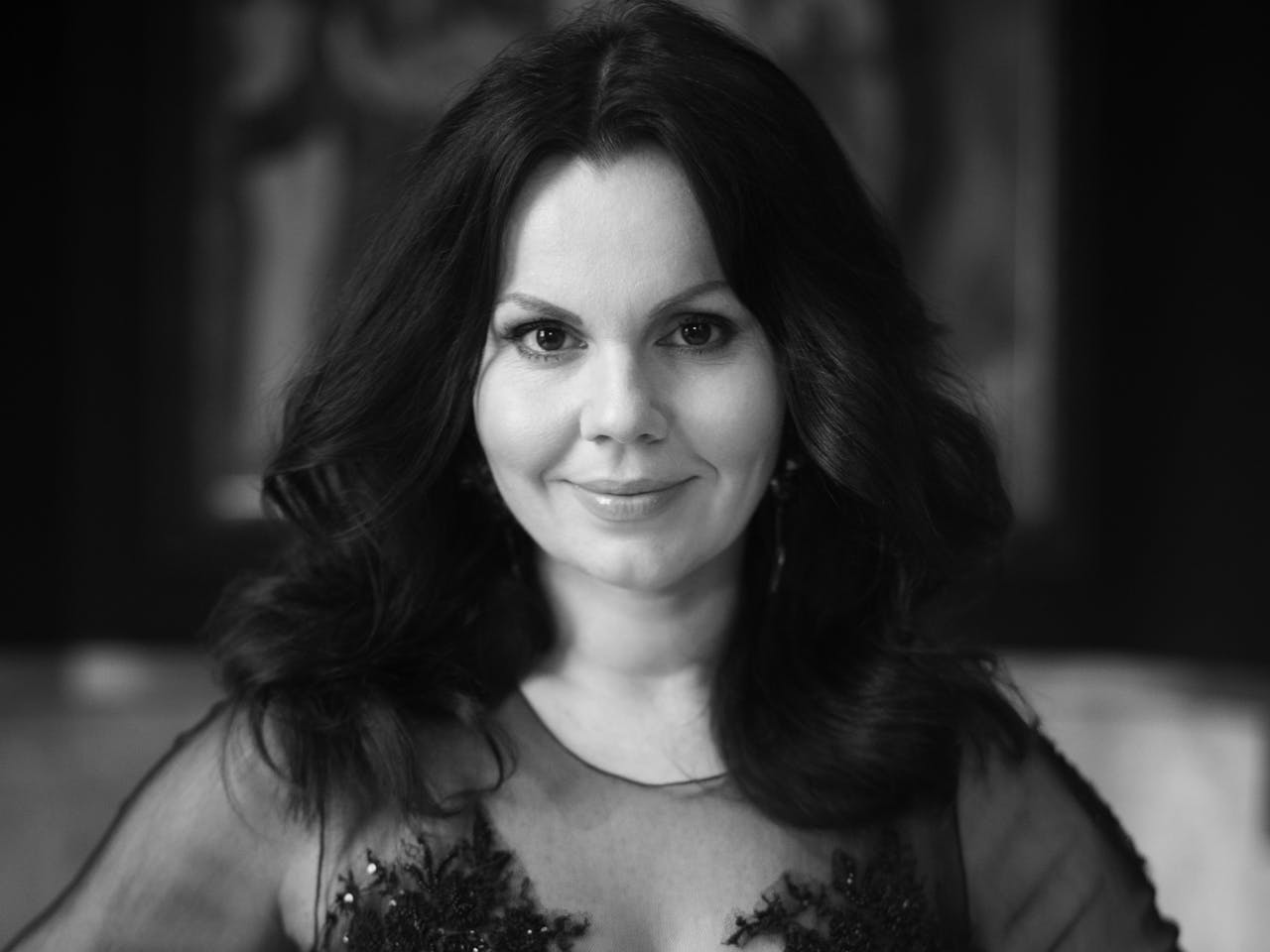 A black and white headshot of the opera singer Aleksandra Kurzak. Her long hair is worn down and she wears a sequinned dress with mesh arms.