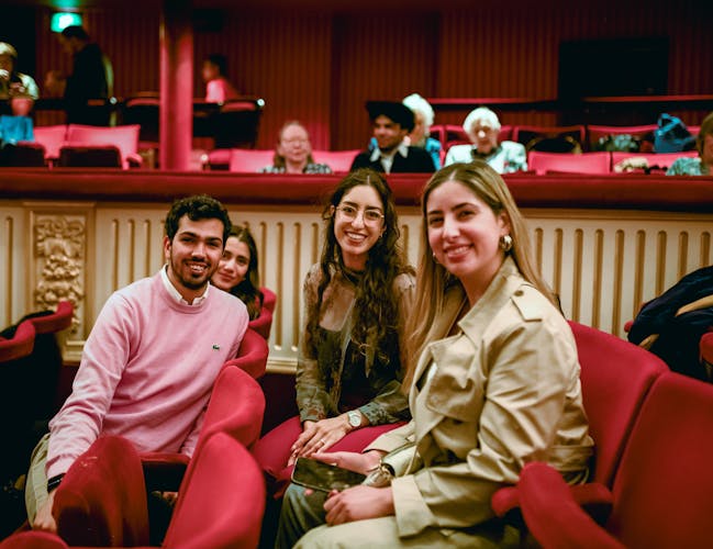 Four people sit in red velvet chairs in the auditorium of the Royal Opera House. They are smiling at the camera.