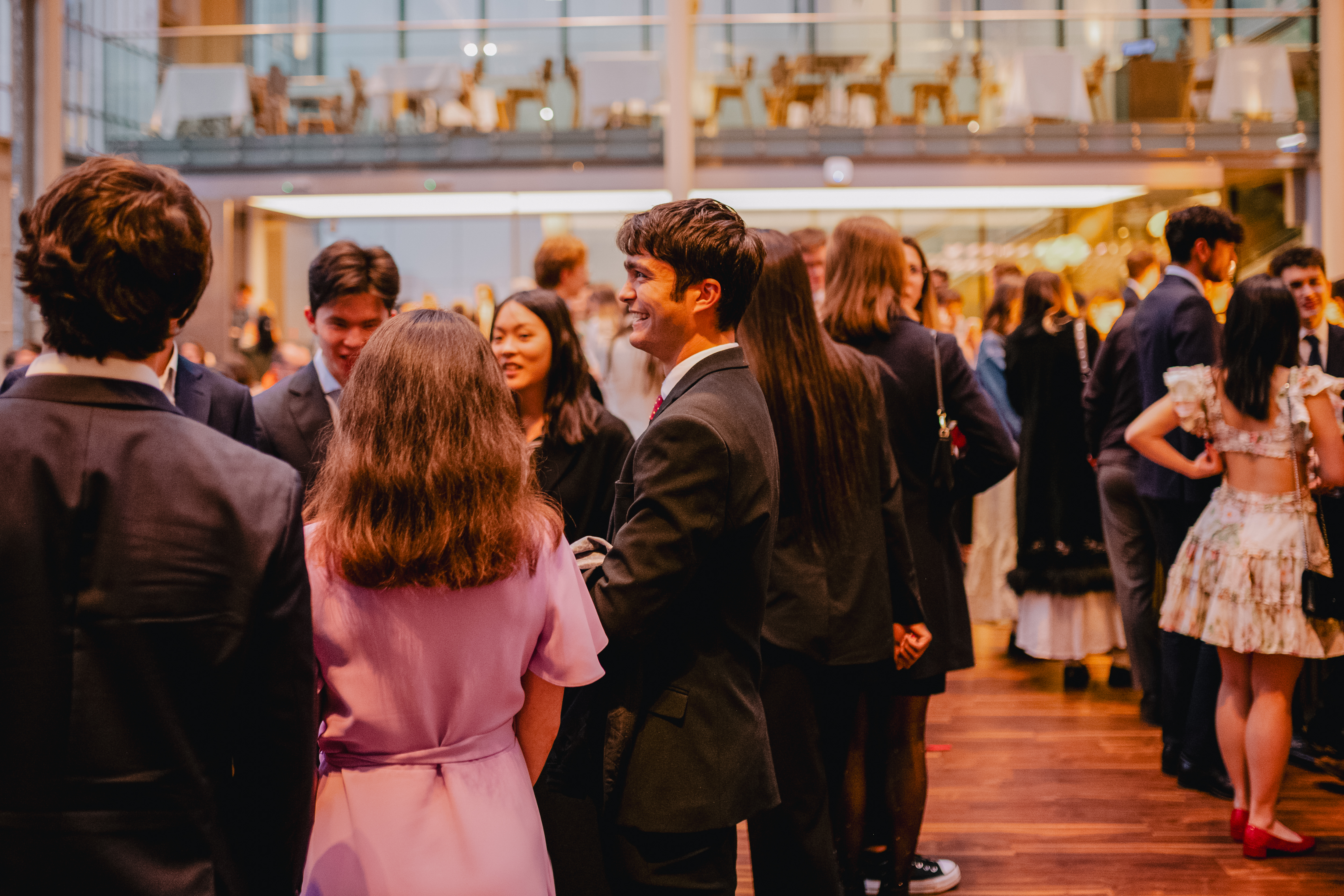 Many people stand in the busy bar area of the Paul Hamlyn Hall in the Royal Opera House in Covent Garden. They are all talking to one another.