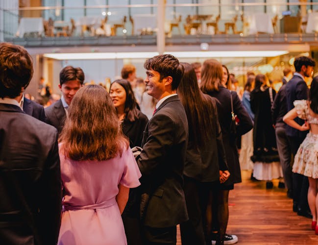 Many people stand in the busy bar area of the Paul Hamlyn Hall in the Royal Opera House in Covent Garden. They are all talking to one another.