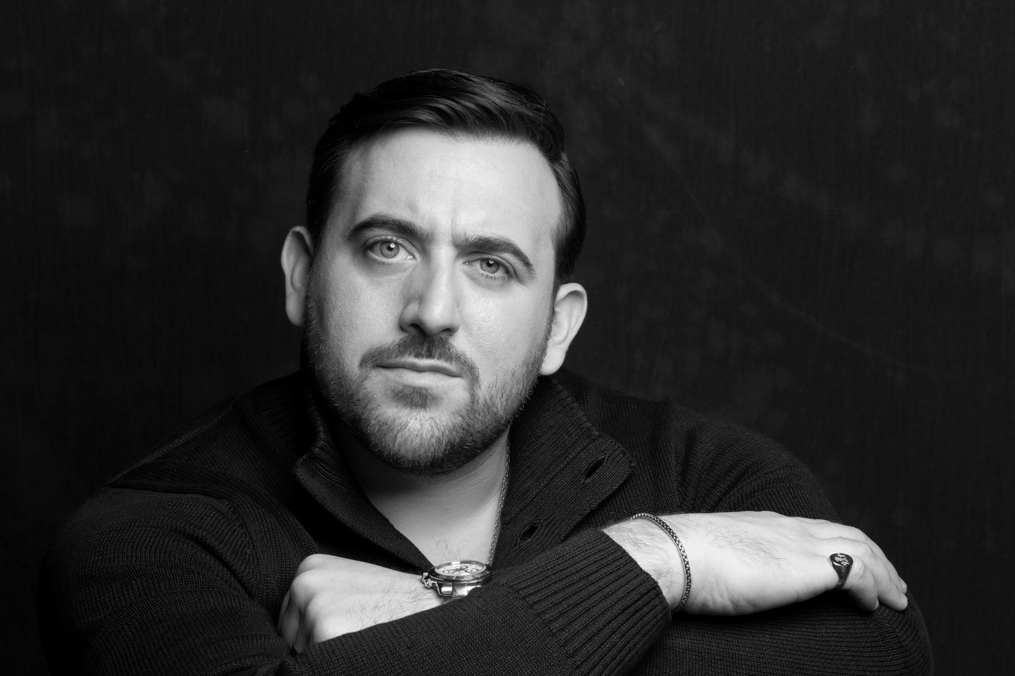 A black and white headshot of the opera singer Freddie de Tommaso. He wears a black jumper and stands against a black backdrop. 