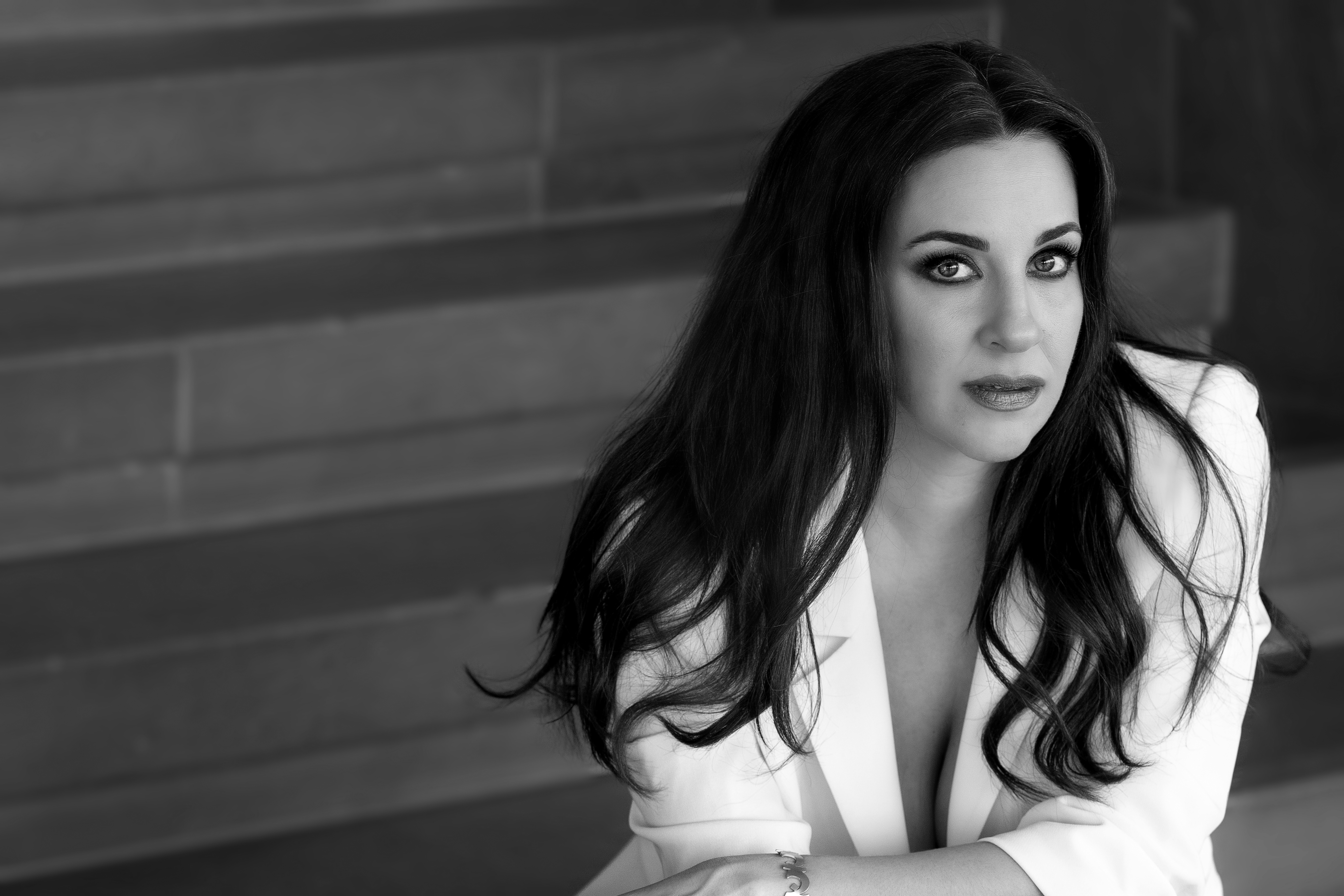 A black and white headshot of the opera singer Joyce El-Khoury. She sits against a brick wall wearing a white suit jacket. 
