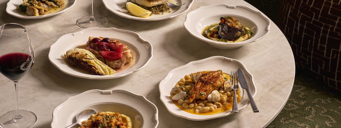 Plates of artfully styled food and glasses of red and white wine are arranged on a round marble table. The display contains menu items from Cicoria, Angela Hartnett's restaurant at the Royal Opera House.