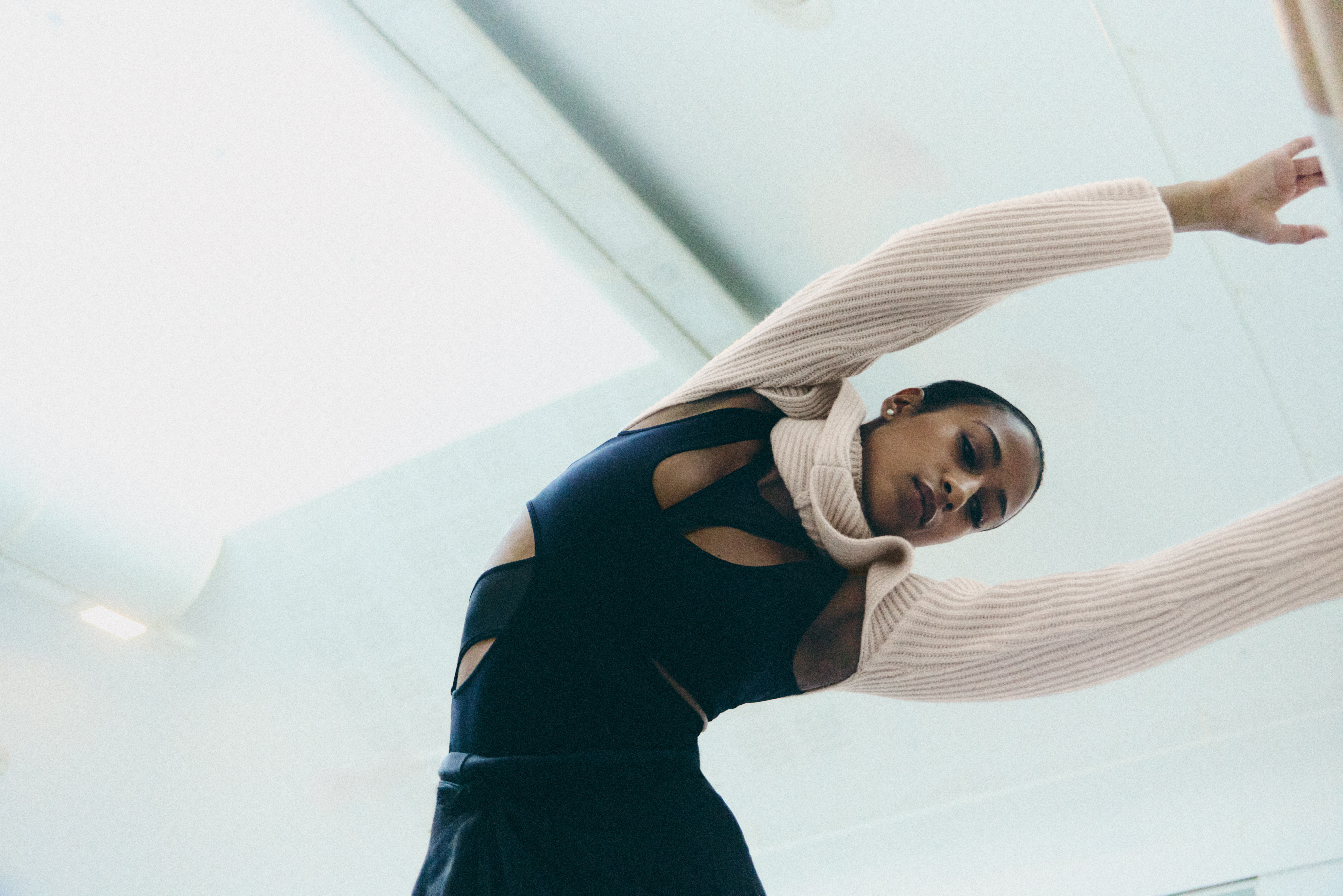 A woman wearing a black sports top and a cream jumper leans her arms over to the left.