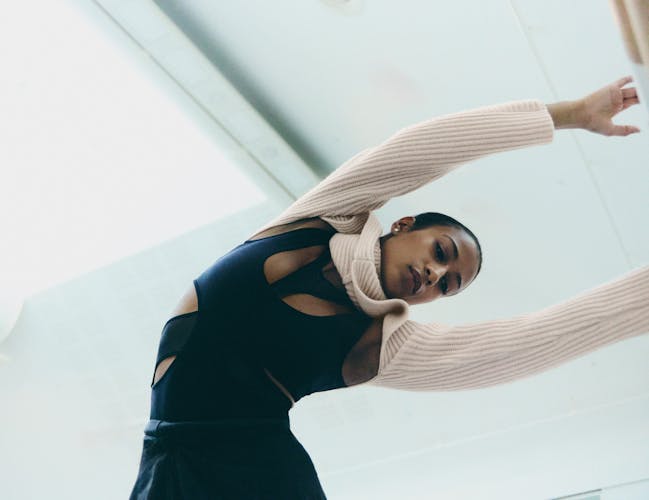 A woman wearing a black sports top and a cream jumper leans her arms over to the left.
