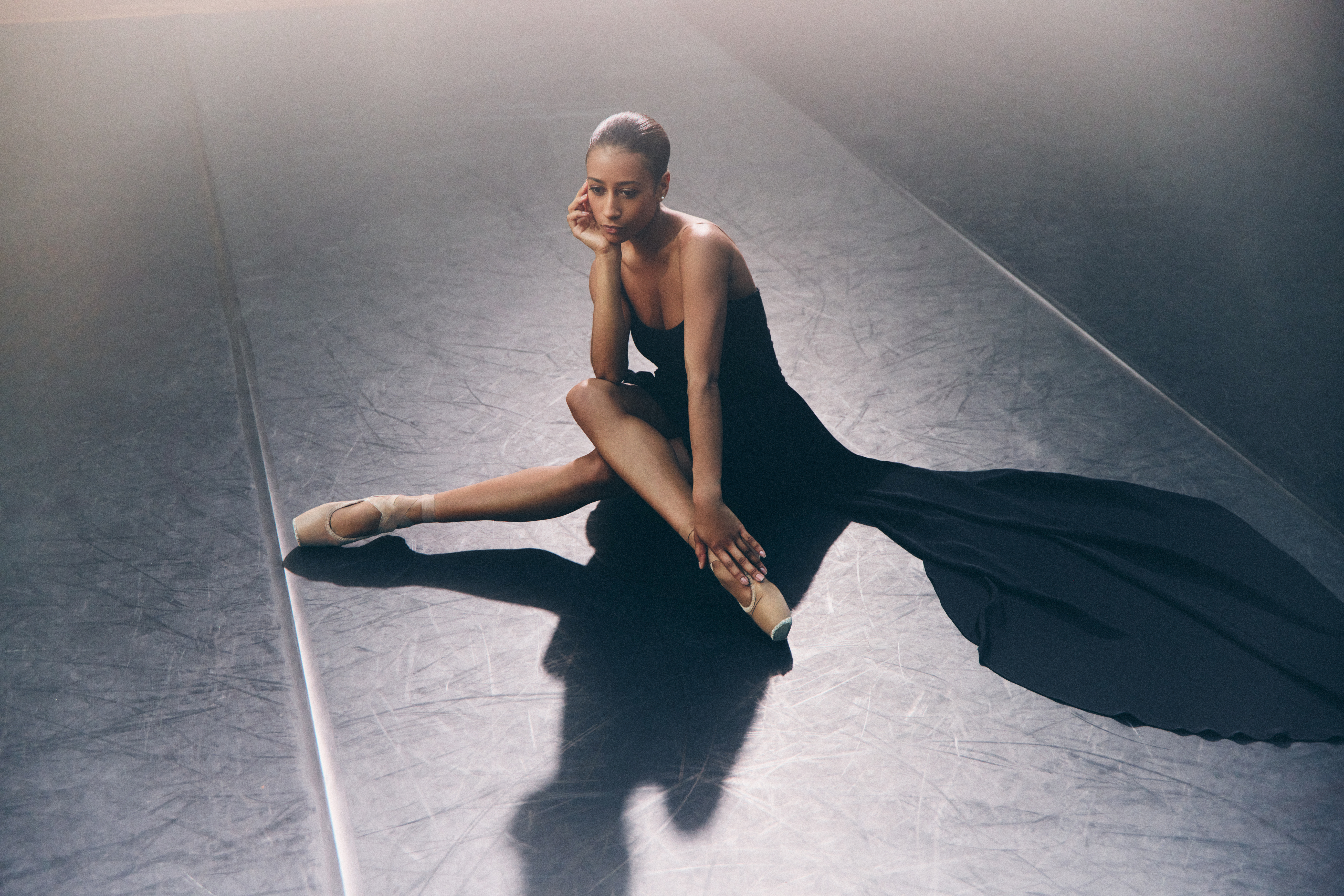 A woman in a black dress sits on the floor.