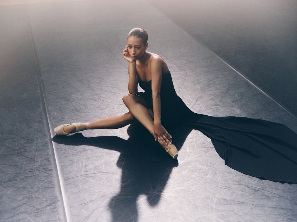 A woman in a black dress sits on the floor.