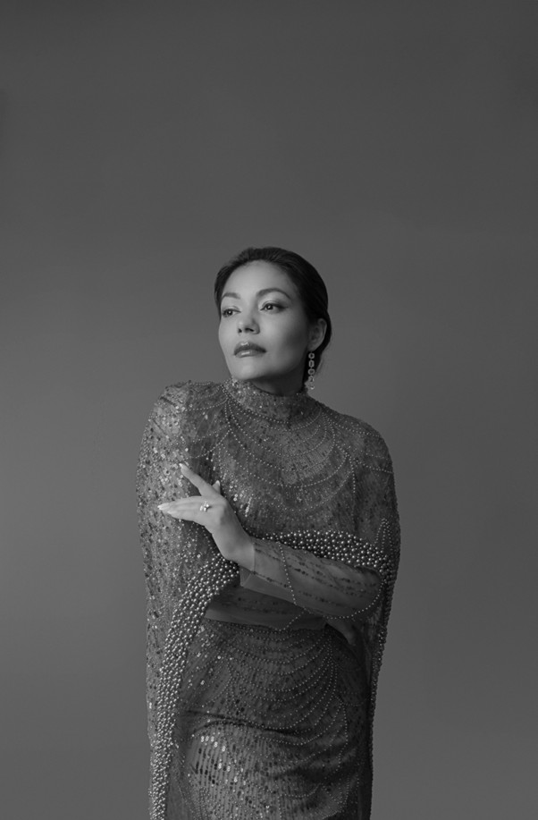 A black and white headshot of the opera singer Ailyn Pérez. She wears a sequinned top. 