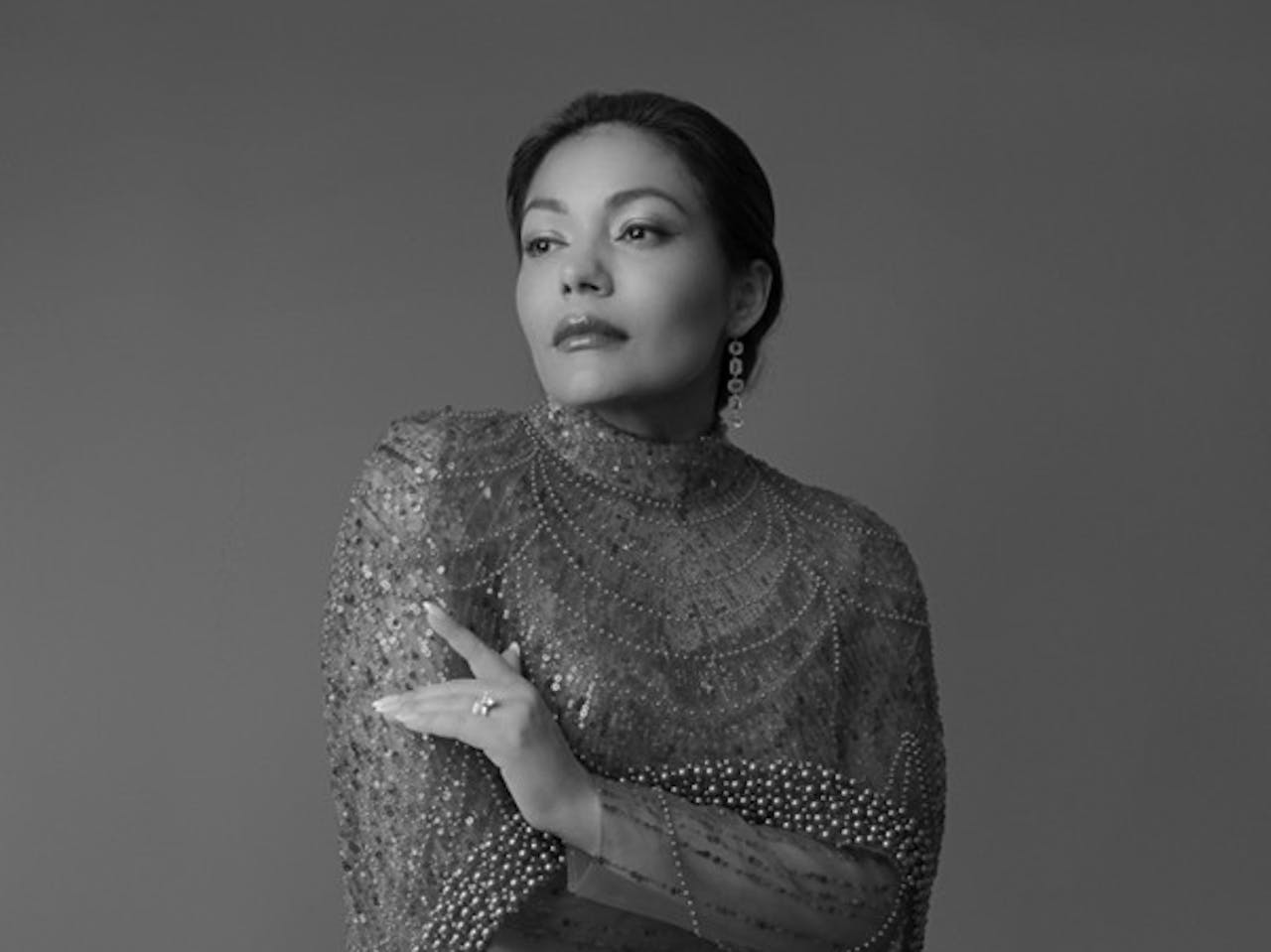 A black and white headshot of the opera singer Ailyn Pérez. She wears a sequinned top.