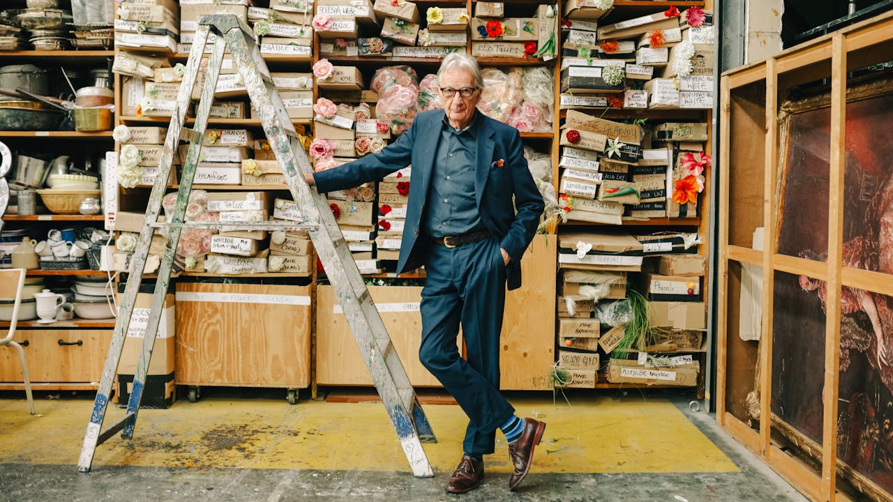 Paul Smith rests against a grey ladder in the Royal Opera House costume workshop ©2025 Kirsty McLachlan