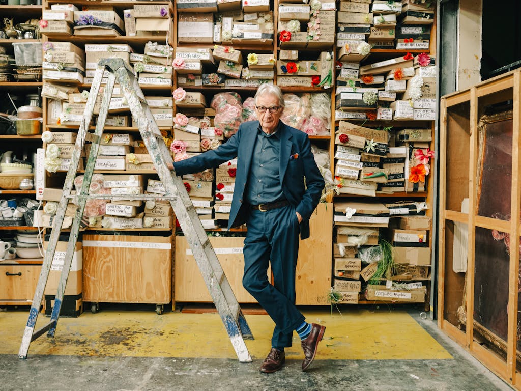 Paul Smith rests against a grey ladder in the Royal Opera House costume workshop ©2025 Kirsty McLachlan