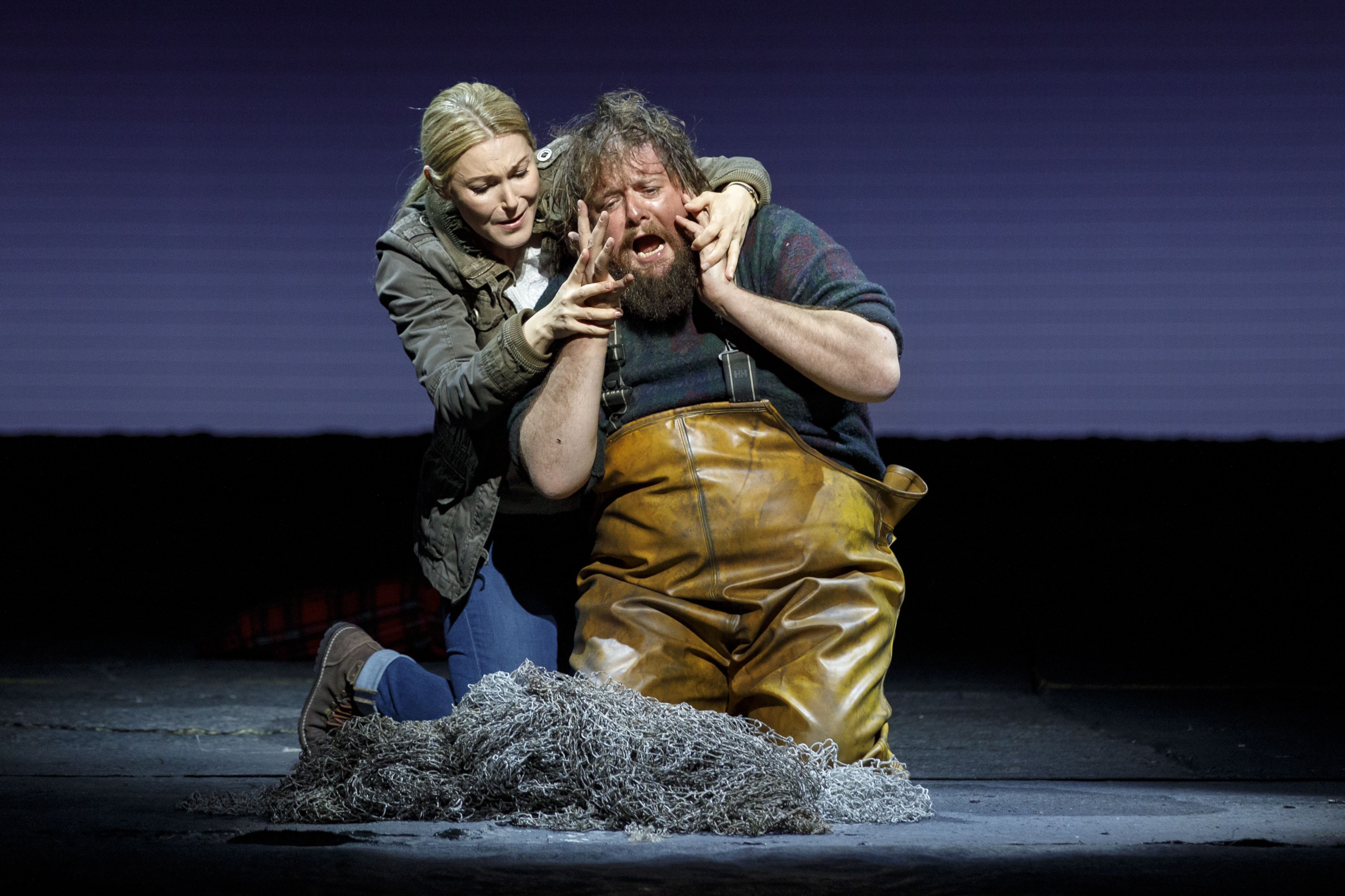 A fisherman despairs on his knees. A woman comforts him from behind, stroking his face.