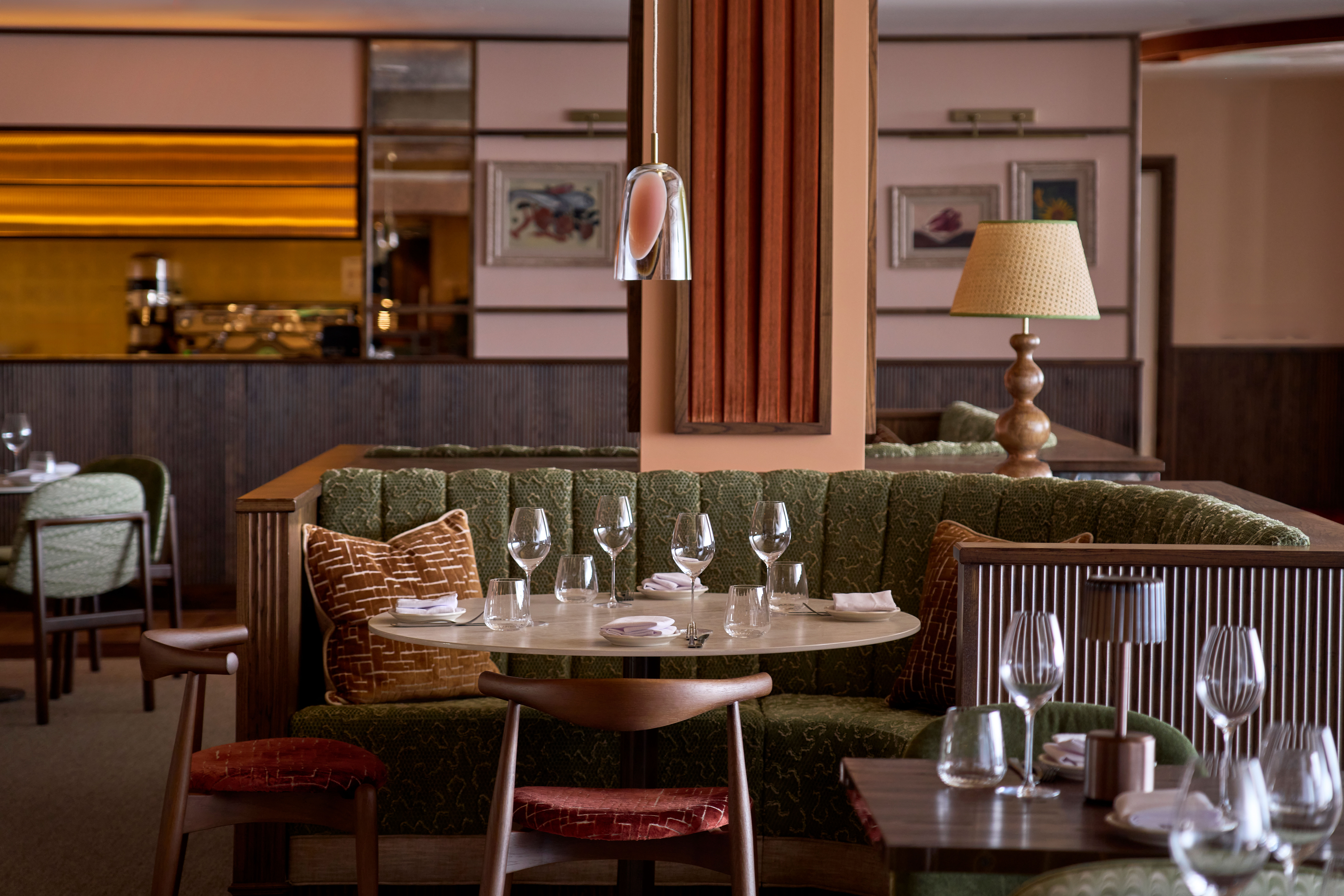 Cozy restaurant interior with plush green booth seating and a round table set with empty wine glasses.