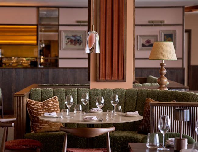 Cozy restaurant interior with plush green booth seating and a round table set with empty wine glasses.