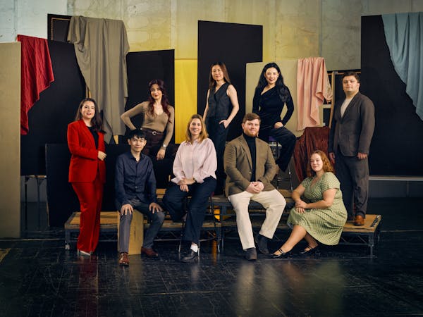 A group of nine people in formal attire pose against a backdrop of hanging fabrics in various colours.