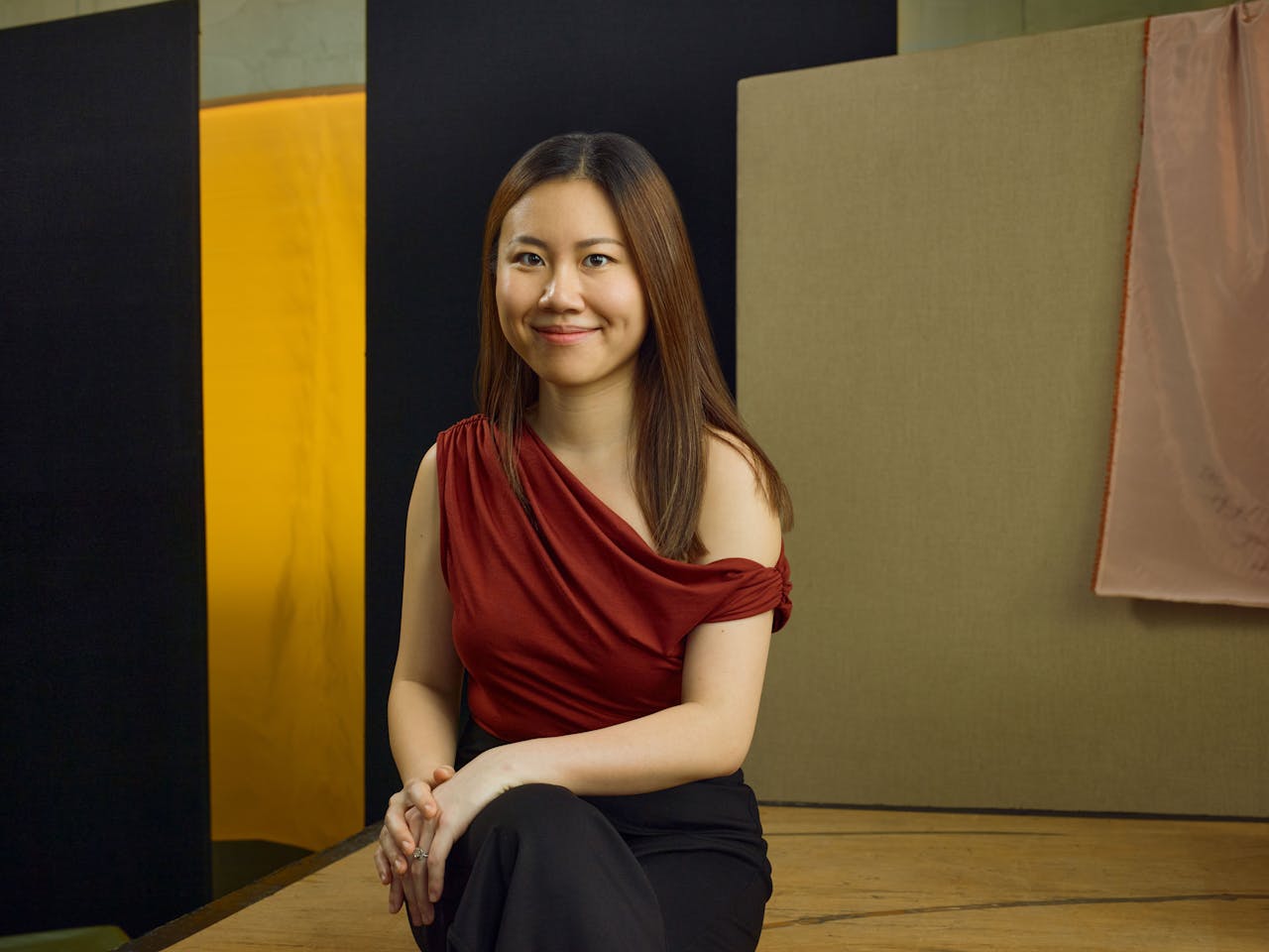 Jette Parker Artist Peggy Wu sits in the centre of the photo, she is wearing a red off the shoulder top and black trousers.