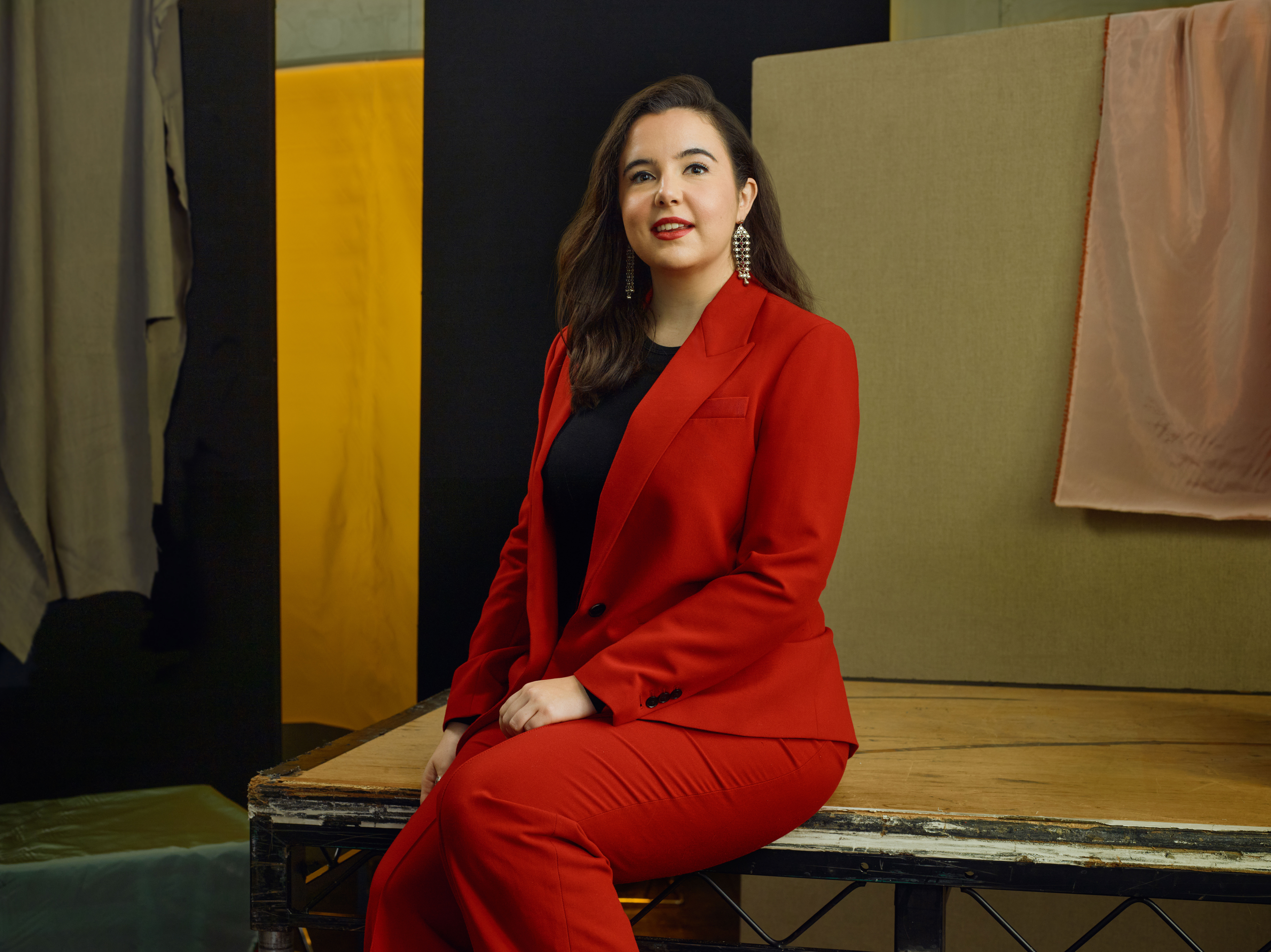 Jette Parker Artist Ellen Pearson sits in the centre of the photo, she is wearing a black t-shirt and red suit jacket and trousers.