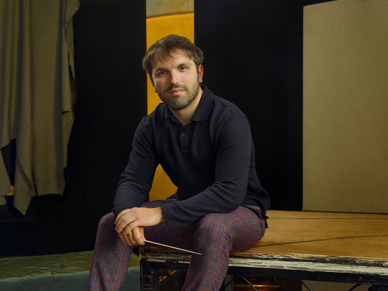 Jette Parker Artist Giovanni Fanizza sits in the centre of the photo, he is wearing a navy long sleeve shirt and dark red and navy plaid trousers.