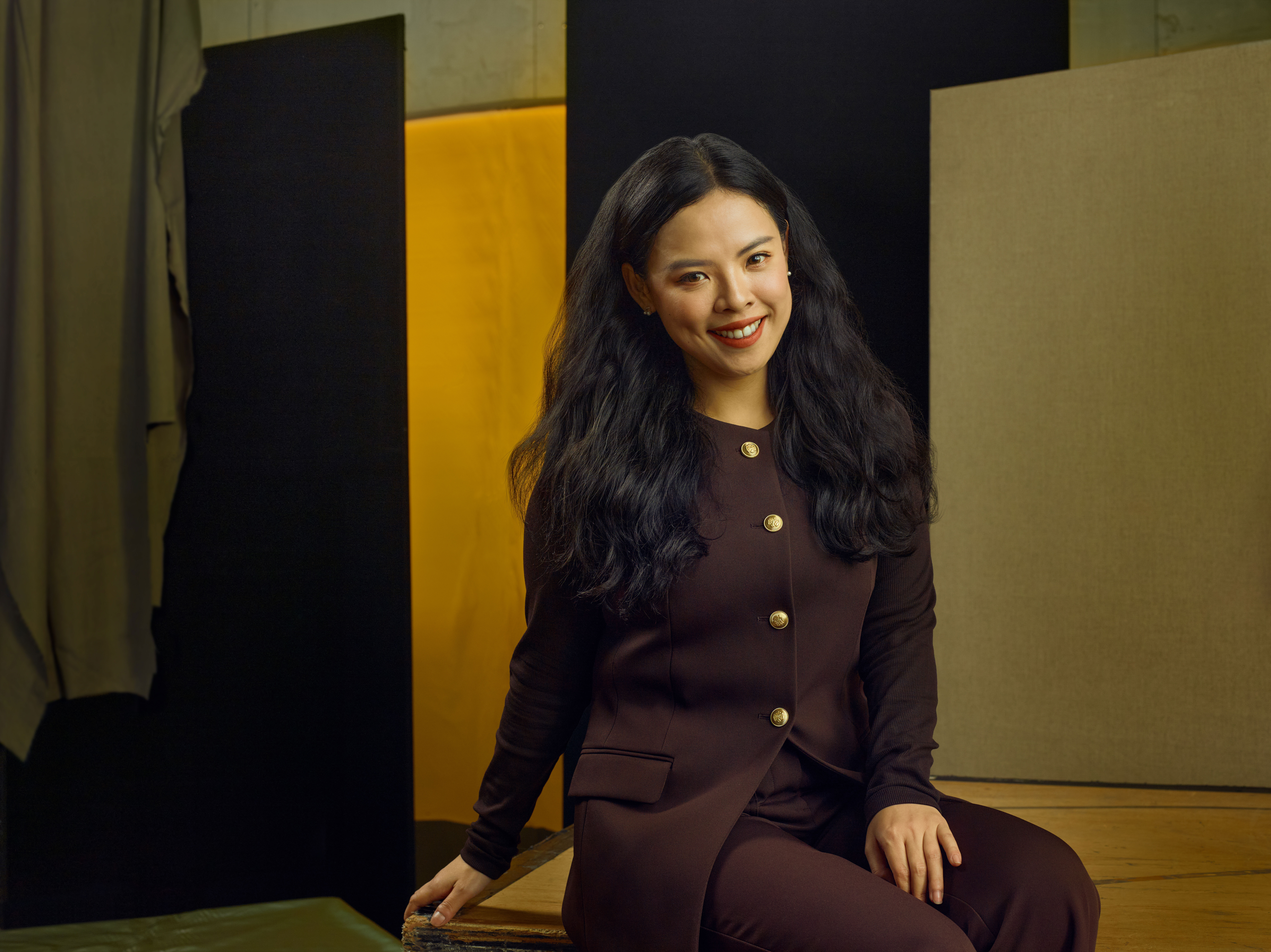 Jette Parker Artist Jingwen Cai sits in the centre of the photo, she is wearing a brown jacket and trousers.