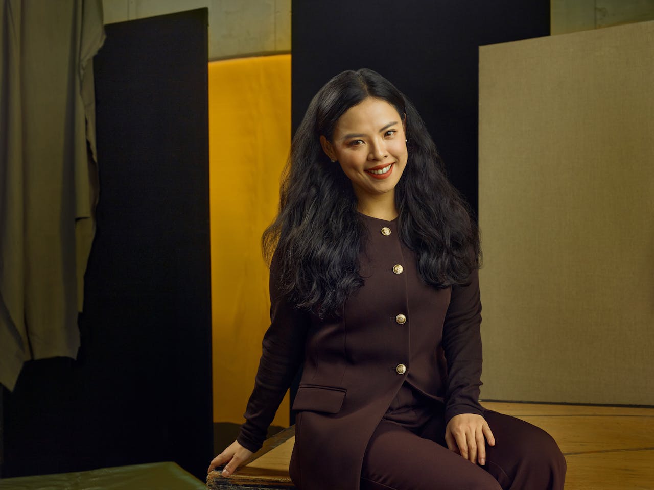 Jette Parker Artist Jingwen Cai sits in the centre of the photo, she is wearing a brown jacket and trousers.