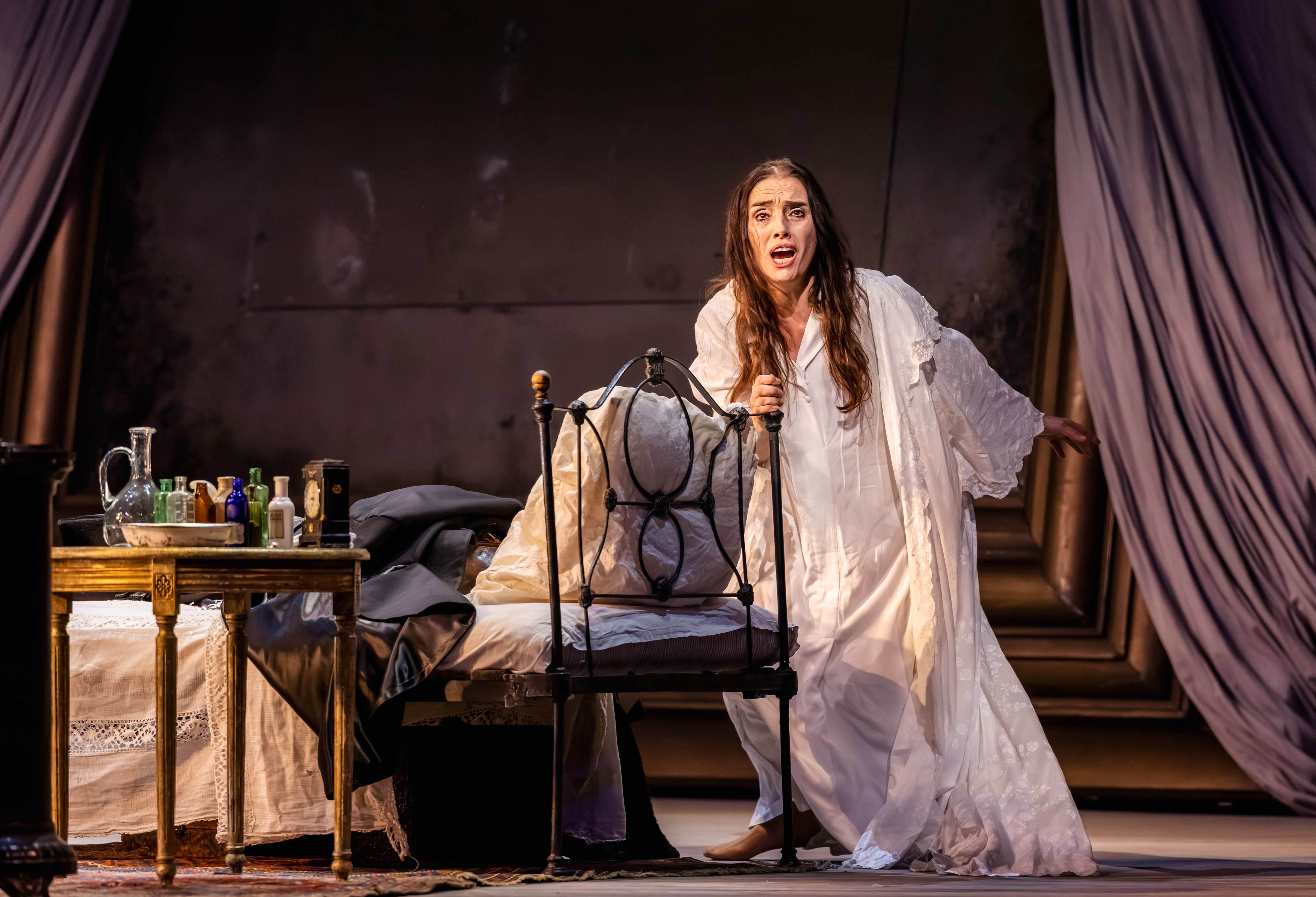 A distressed woman in a white gown holds on to a iron chair.