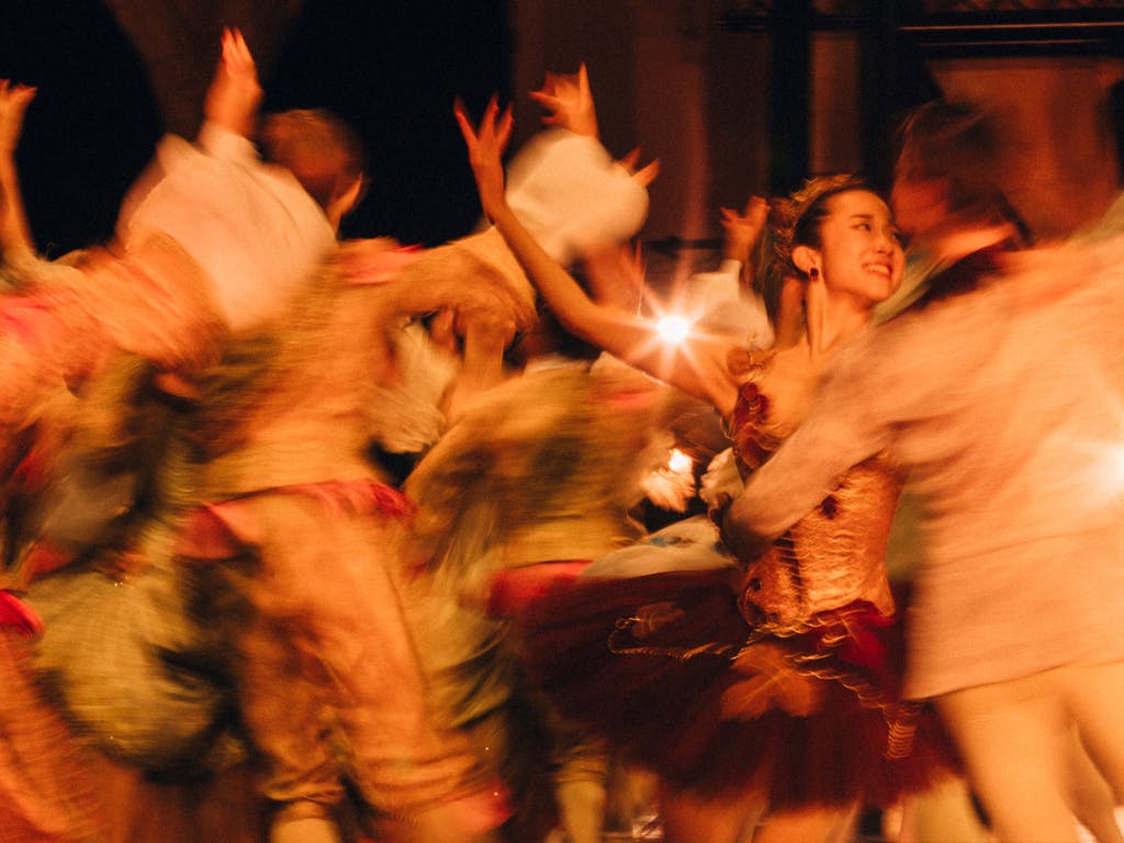 Dancers in costume perform on stage, they are blurred as they move.