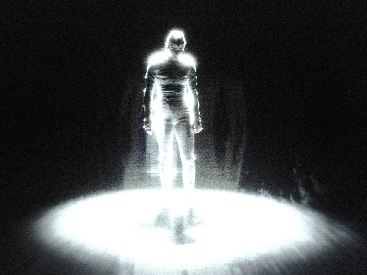 A figure stands in a spotlight of light. Around him is darkness.