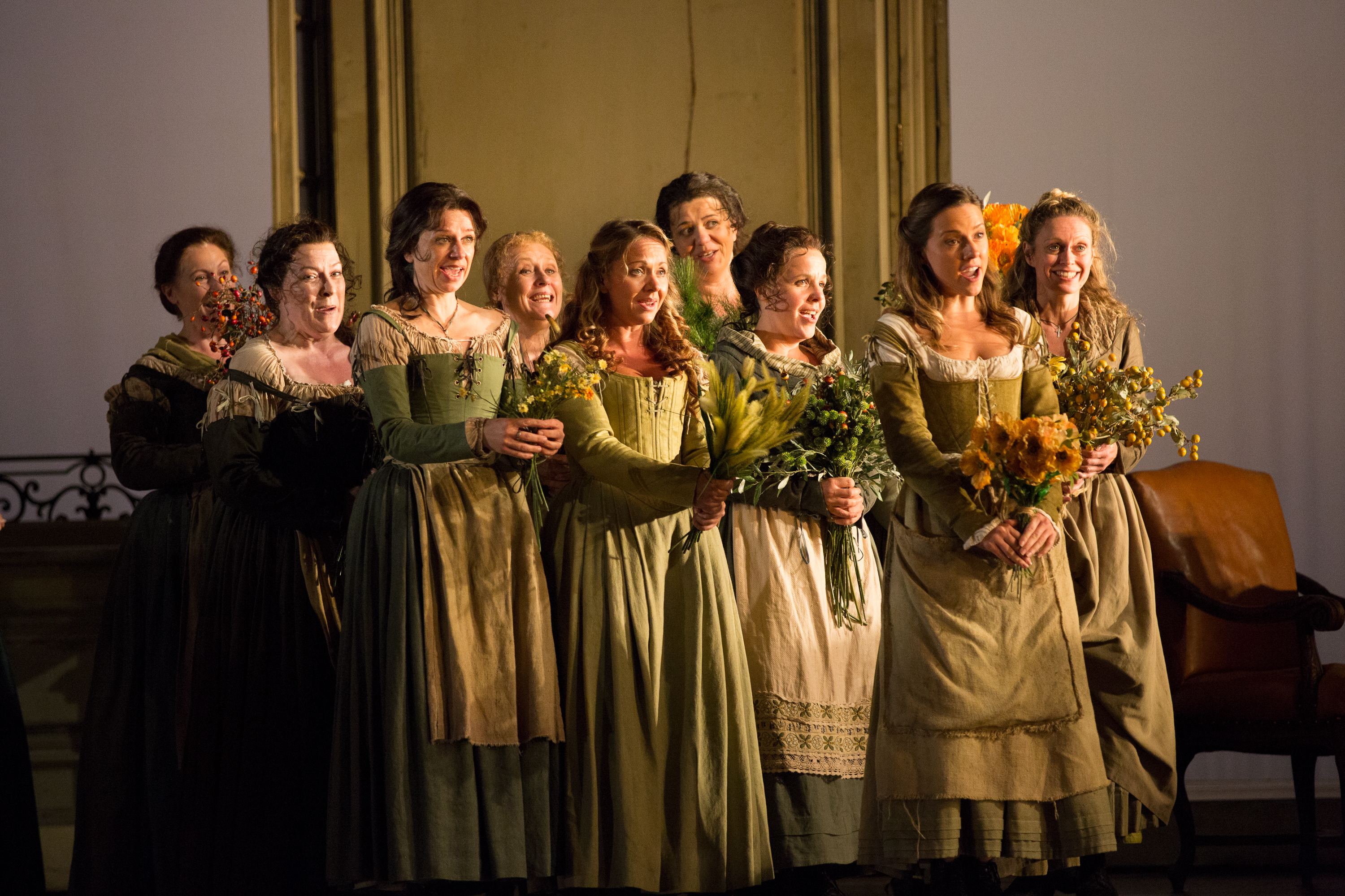 A group of women in green dresses holding bouquets of flowers and singing. 