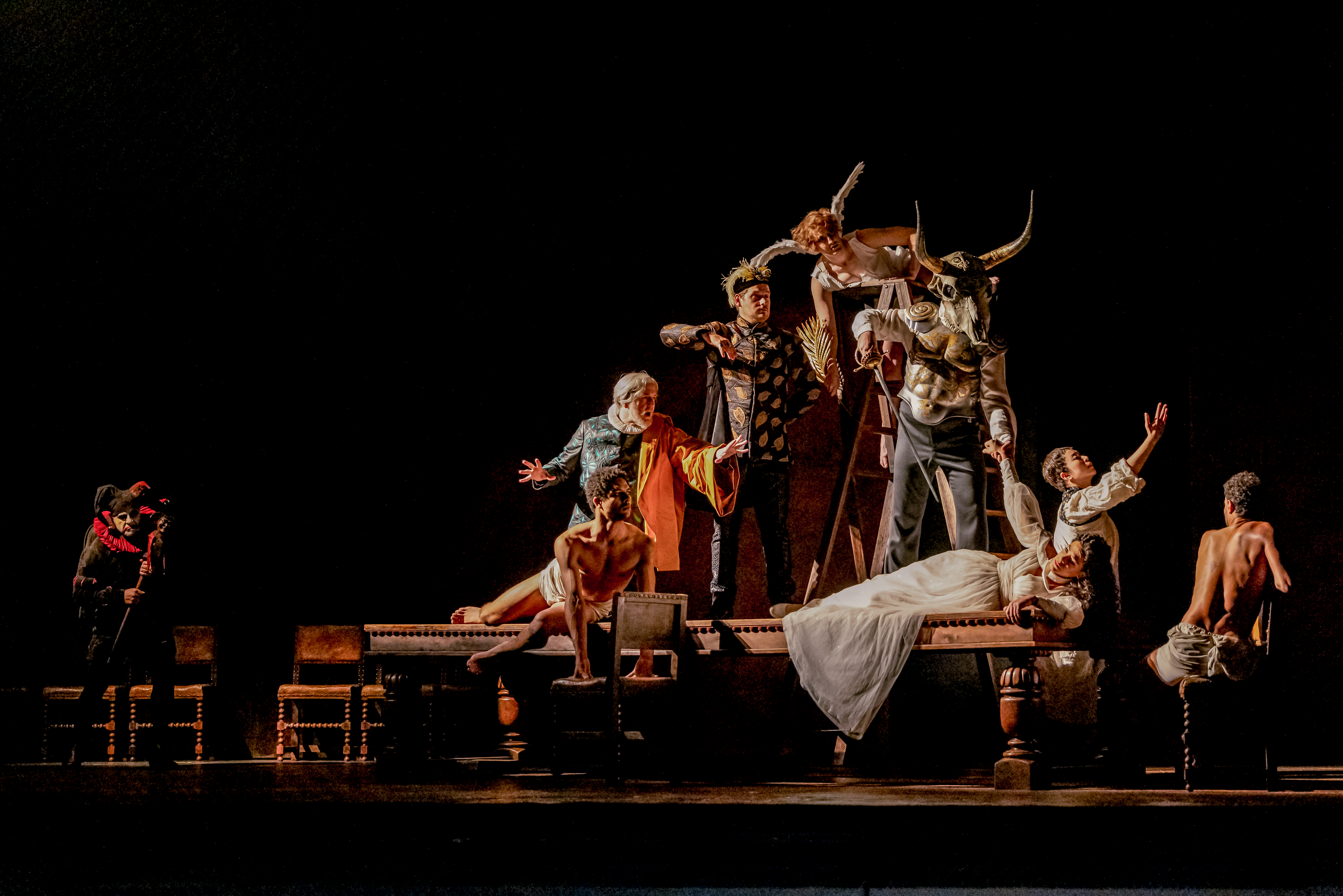 A tableau of a woman in white lying on a table as figures loom above her. There is a minotaur, an angel and a scholar. 