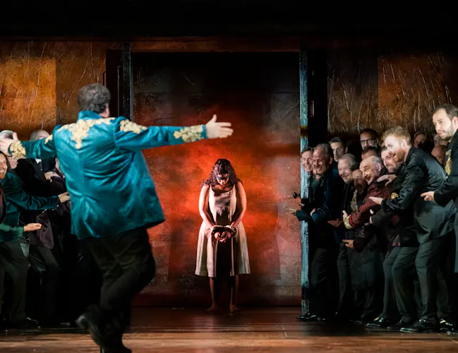 A man holds his arms wide in welcome for a woman who is standing through a set of doors.