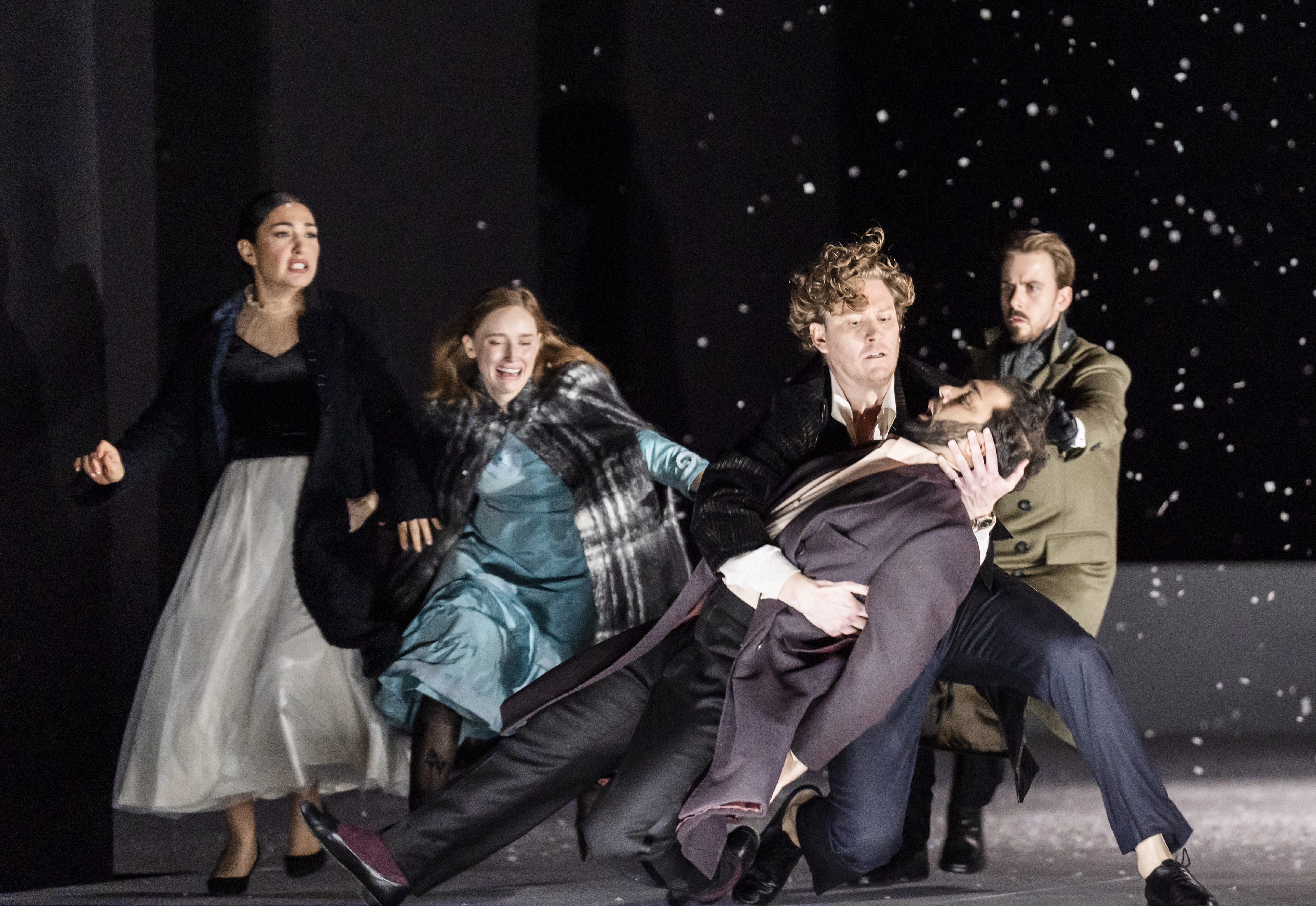 A man has been shot and falls into his friends arms. Behind them, their other friends run forwards. There is snow falling. 