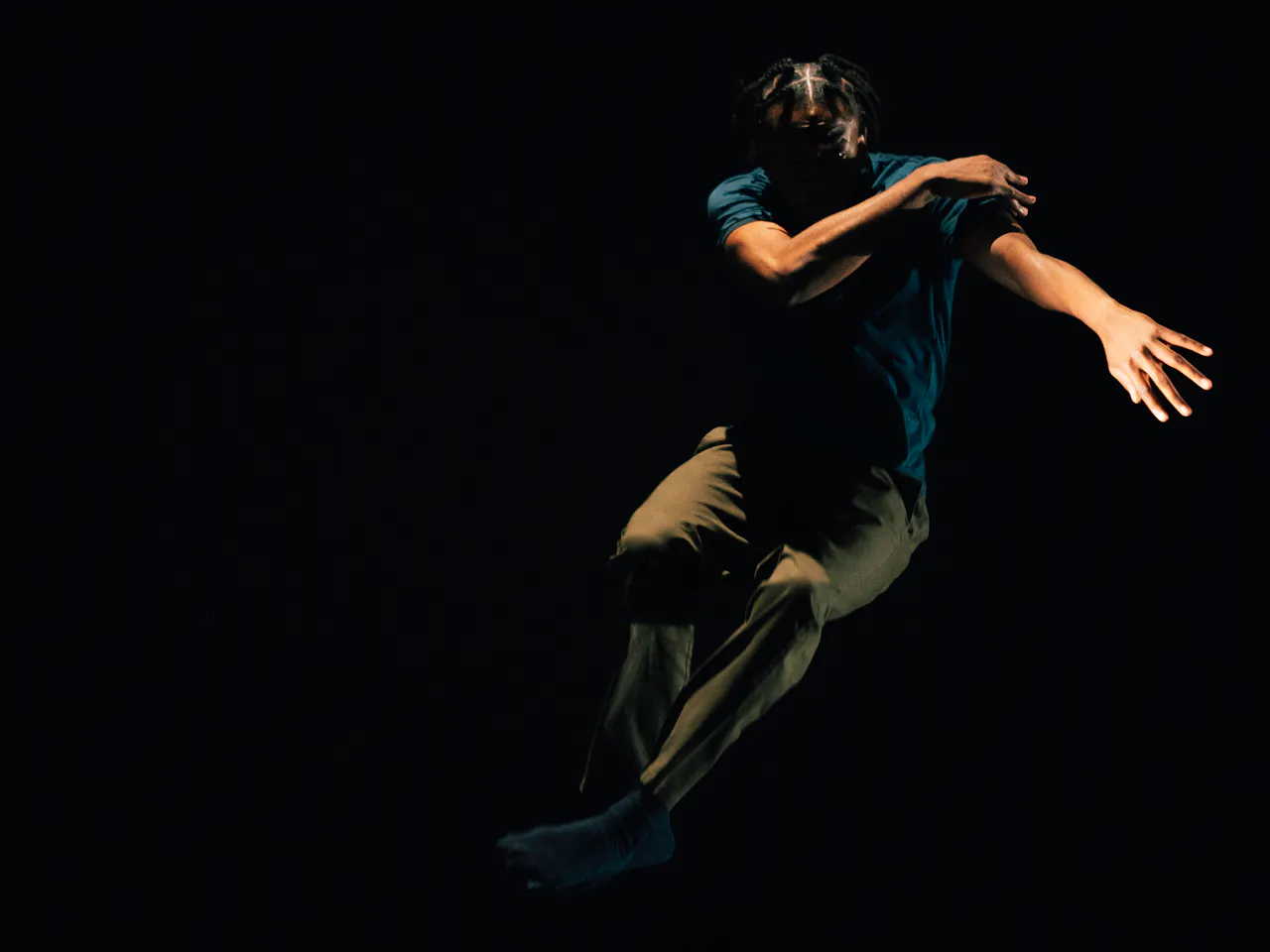 A dancer is mid-air against a dark backdrop, his arms cover his face.