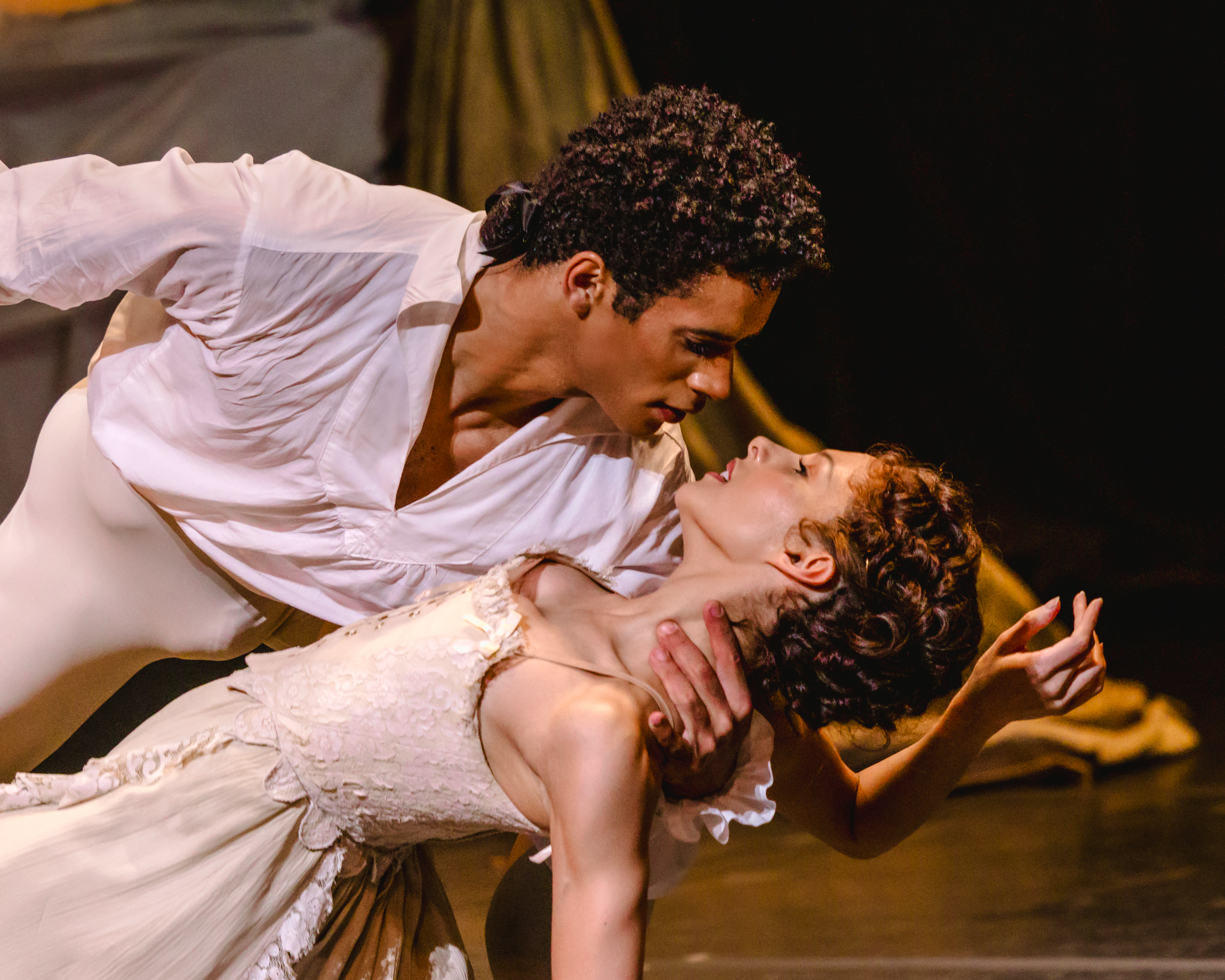 A ballet dancer wearing white passionately holds a ballet dancer wearing a white dress by her neck as they stare into each other eyes. (8 of 10)