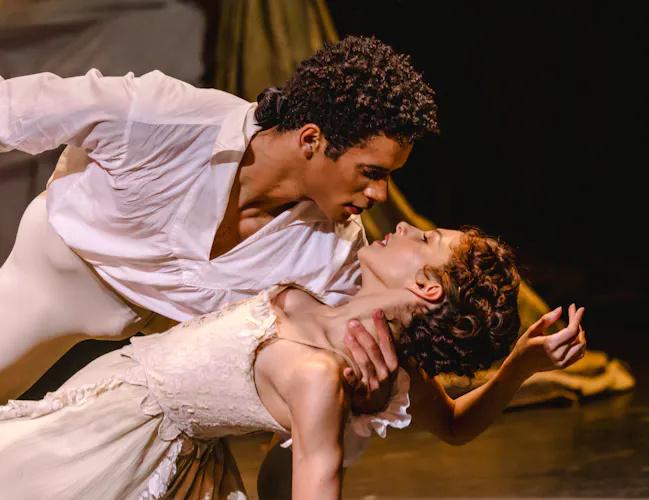 A ballet dancer wearing white passionately holds a ballet dancer wearing a white dress by her neck as they stare into each other eyes. (8 of 10)