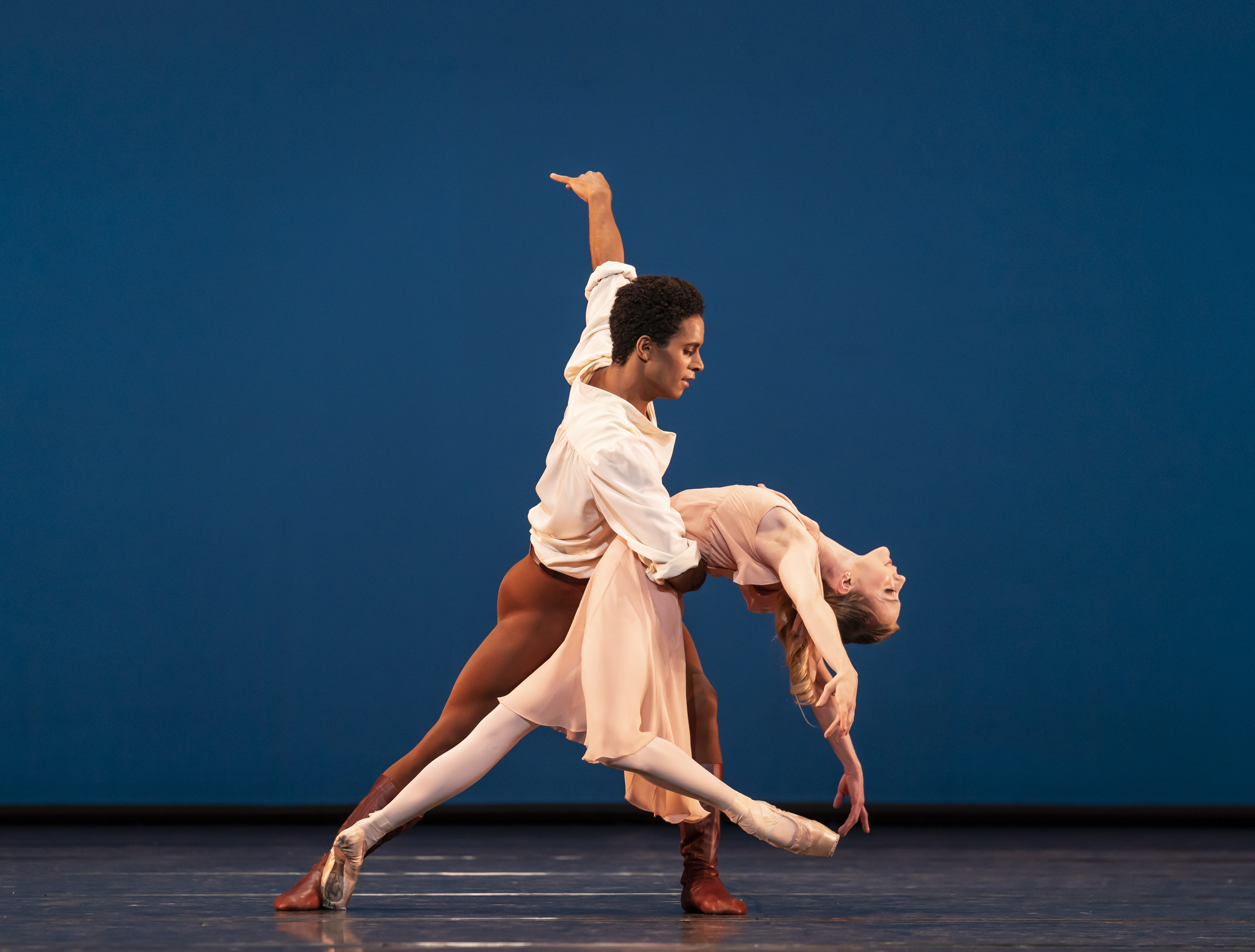 Two ballet dancers perform together on a stage with a bright blue backdrop. (3 of 6)