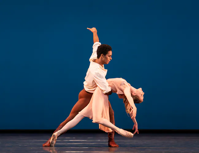 Two ballet dancers perform together on a stage with a bright blue backdrop. (3 of 6)