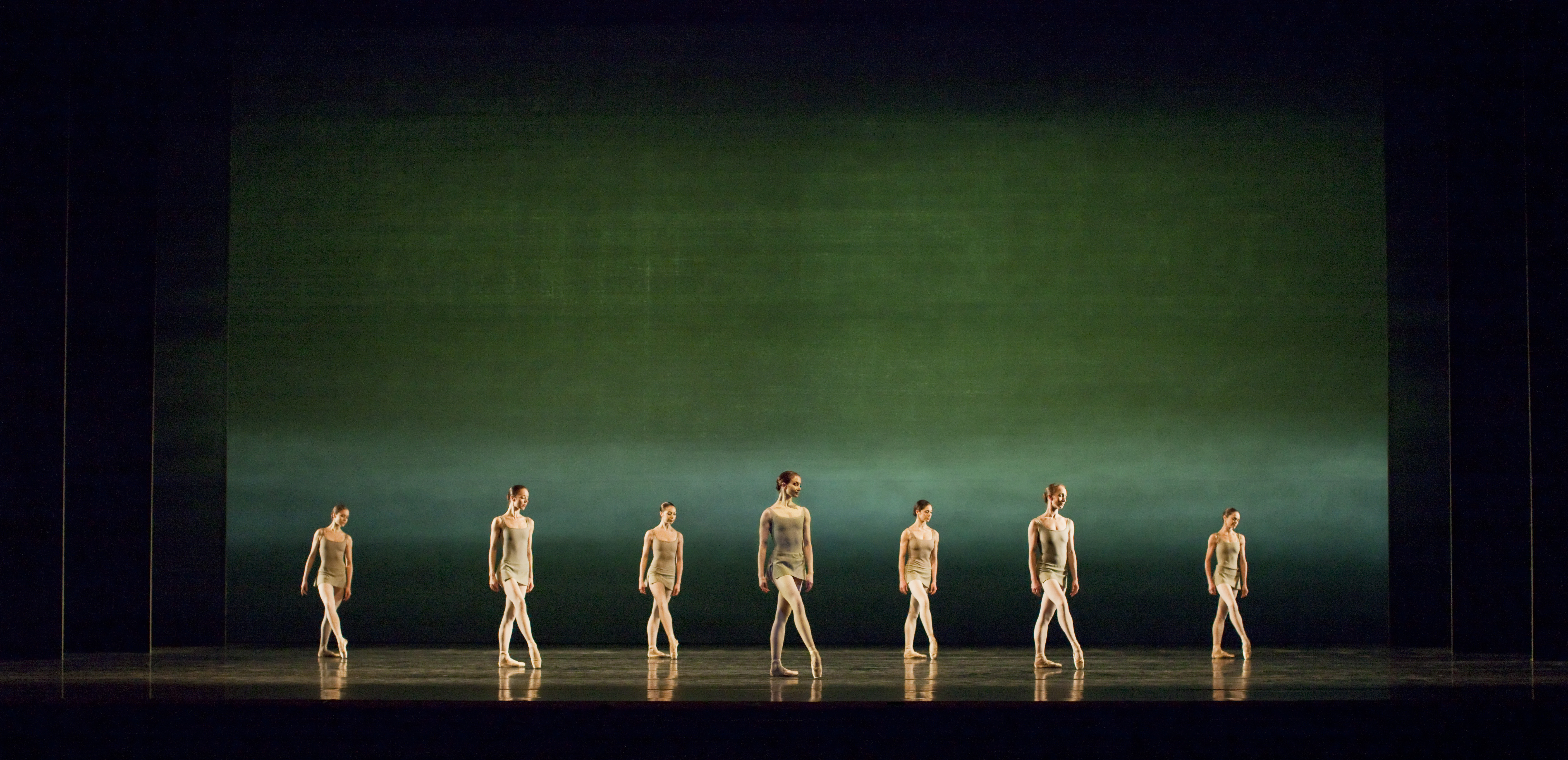 Several ballet dancers stand en pointe on a stage lit with a gradient green backdrop. (6 of 6)