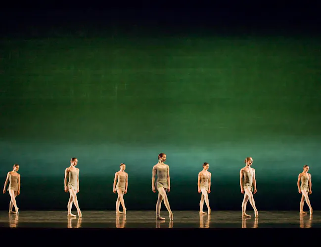 Several ballet dancers stand en pointe on a stage lit with a gradient green backdrop. (6 of 6)