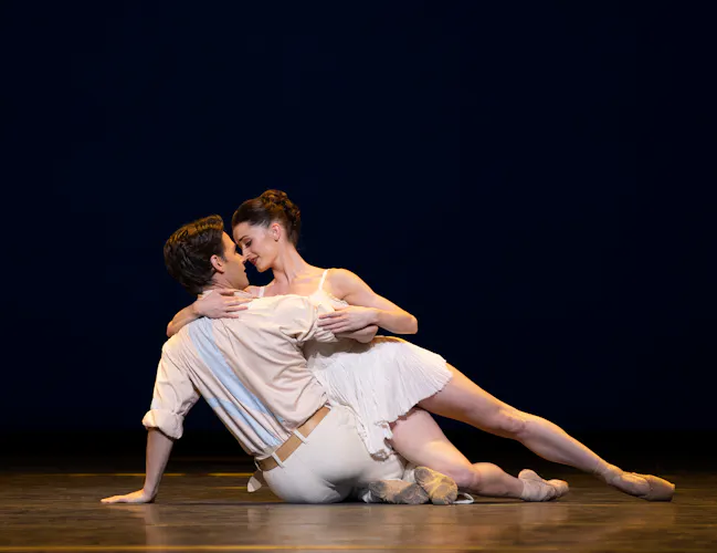 Two ballet dancers lie in a passionate embrace on the floor of a stage with a dark background. (6 of 6)