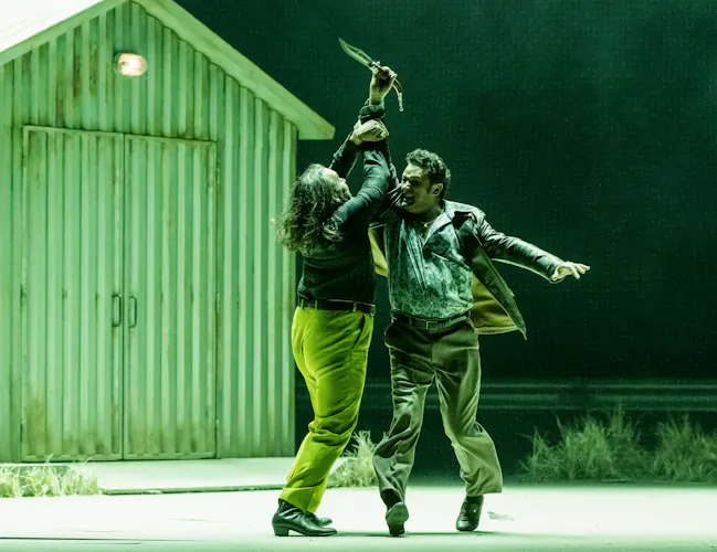 Two performers fight on stage with one raising a knife into the air. They are performing in The Royal Opera's production of Carmen. (6 of 7)