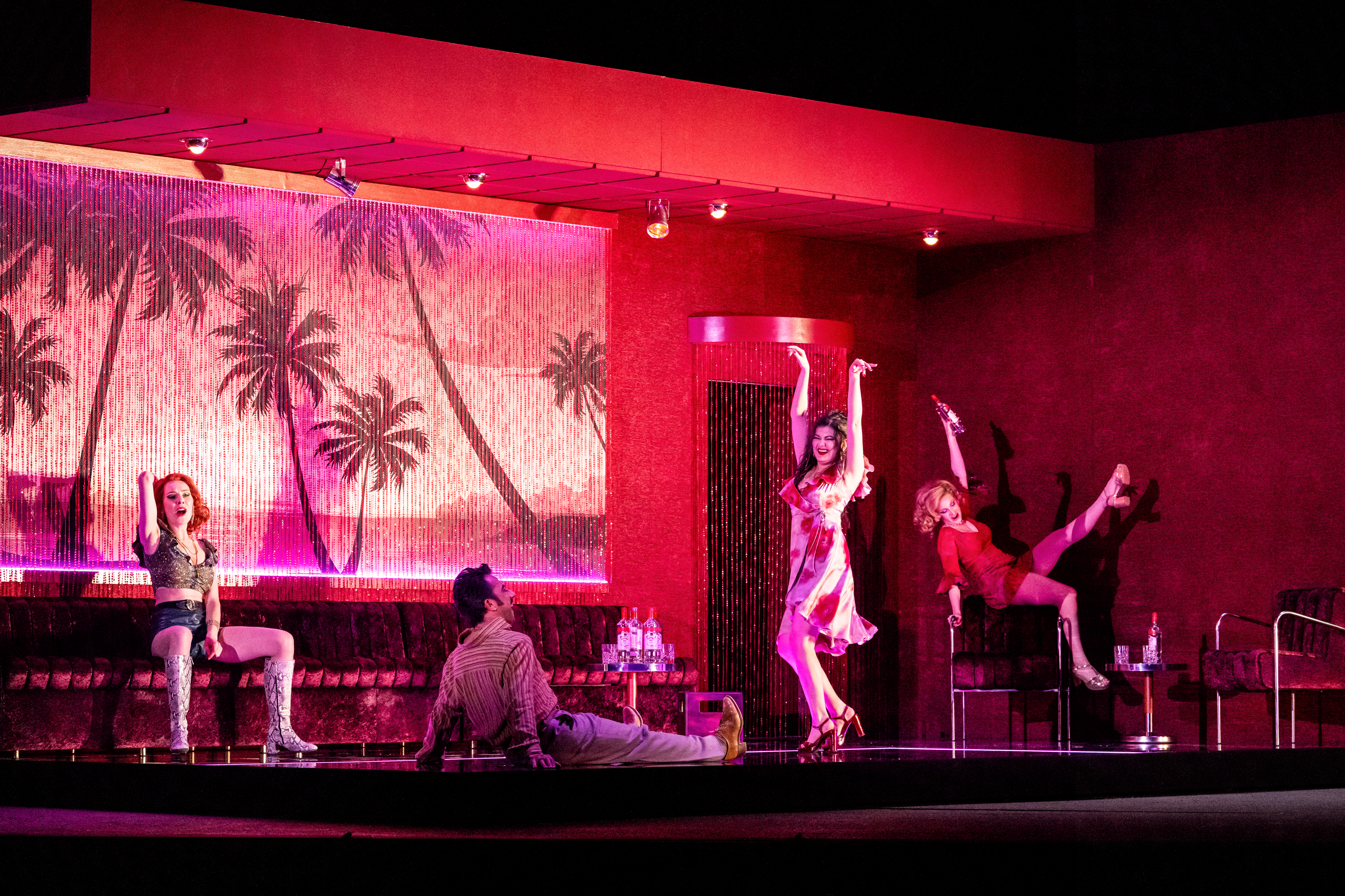 A bar scene on a stage with pink and red neon lighting and several performers dancing. They are performing in The Royal Opera's production of Carmen. (7 of 7)