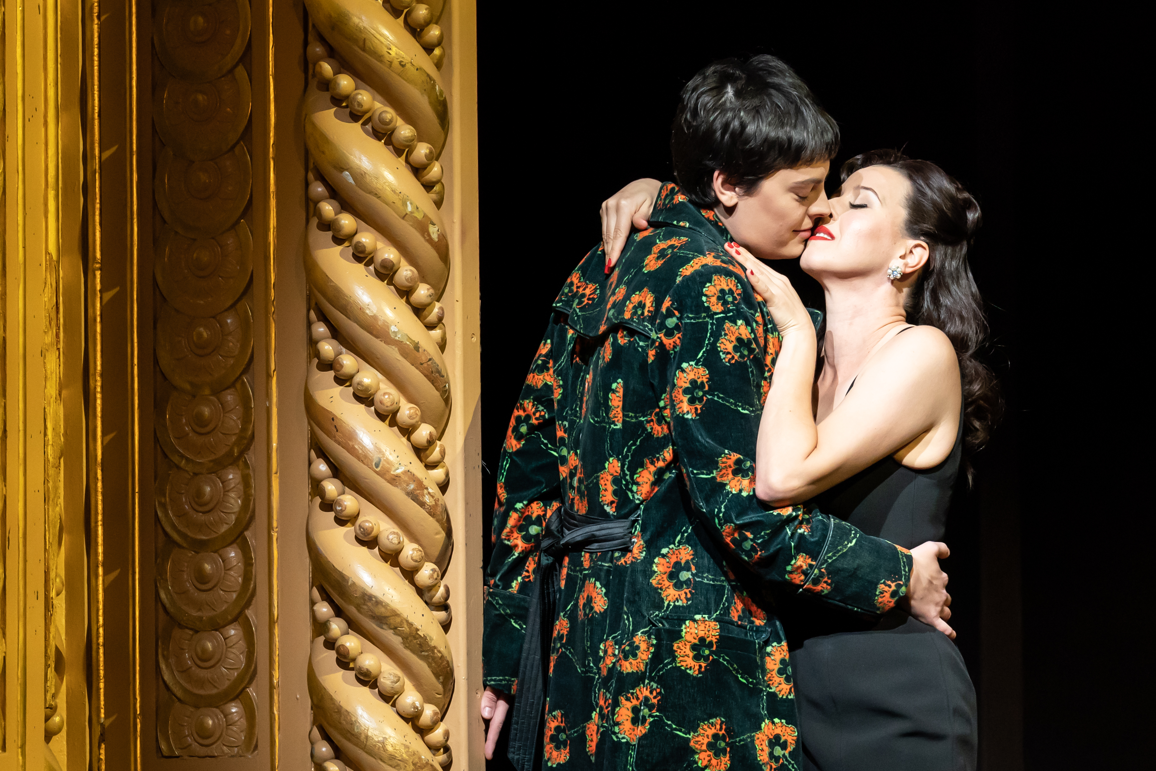 Two performers embrace passionately next to an ornate gilded gold column on stage of The Royal Opera House in a production of Alcina. (2 of 6)