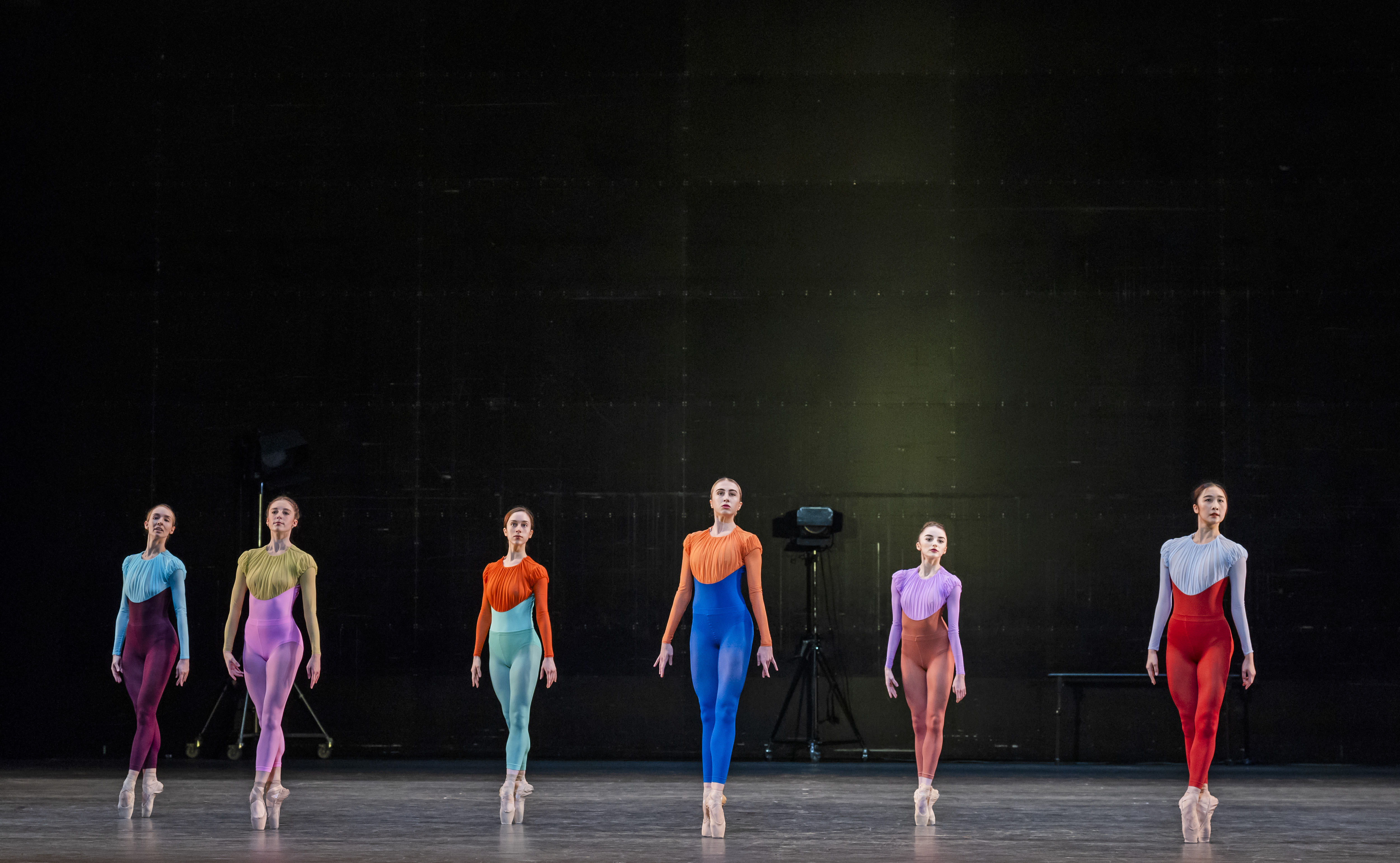 Several ballet dancers wear brightly coloured long-legged leotards on a stark stage. (3 of 8)