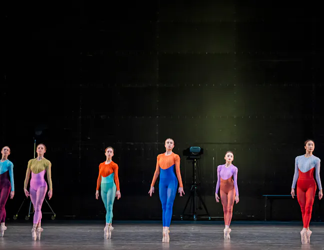Several ballet dancers wear brightly coloured long-legged leotards on a stark stage. (3 of 8)