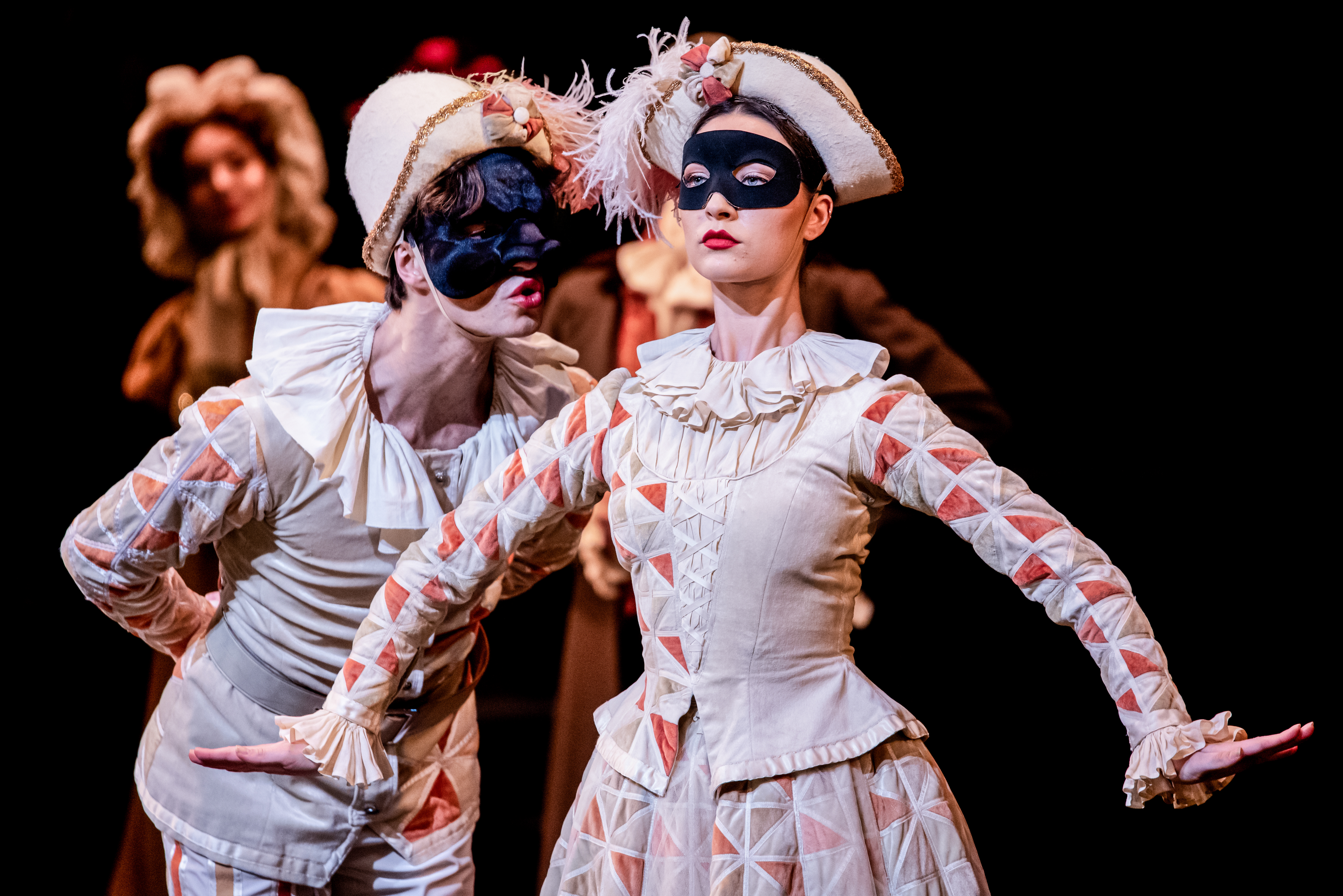 Two ballet dancers wearing a harlequin costumes, feather capped hats and black eye masks perform on stage. It is a scene from The Royal Opera House in The Royal Ballet's production of The Nutcracker. (2 of 5)